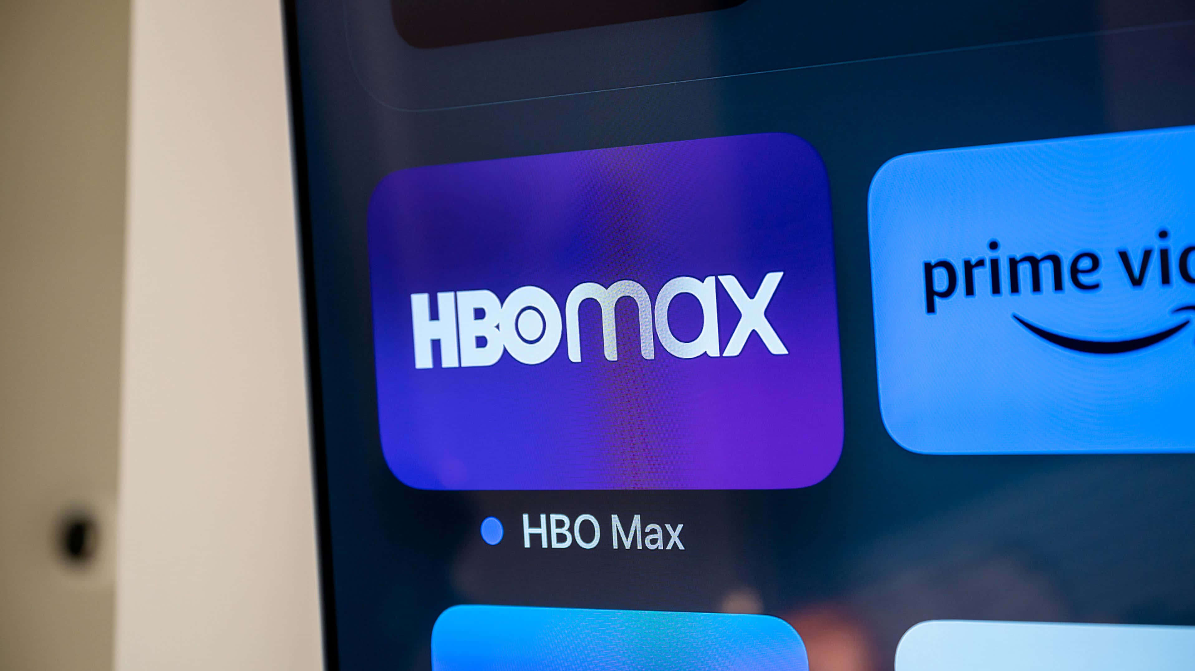 與家人一起享受HBO的電影之夜 壁紙 — HBO Max 應用程式圖示在串流服務主畫面上發出紫色光芒的特寫，旁邊可見 Prime Video。