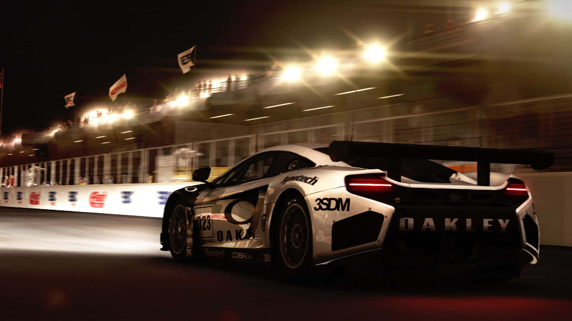 HD Grid Autosport 賽車操控背景 壁紙 — 一輛帶有Oakley品牌標誌的白色賽車在明亮的體育場燈光下，於夜間賽道上高速行駛，帶有動態模糊效果。