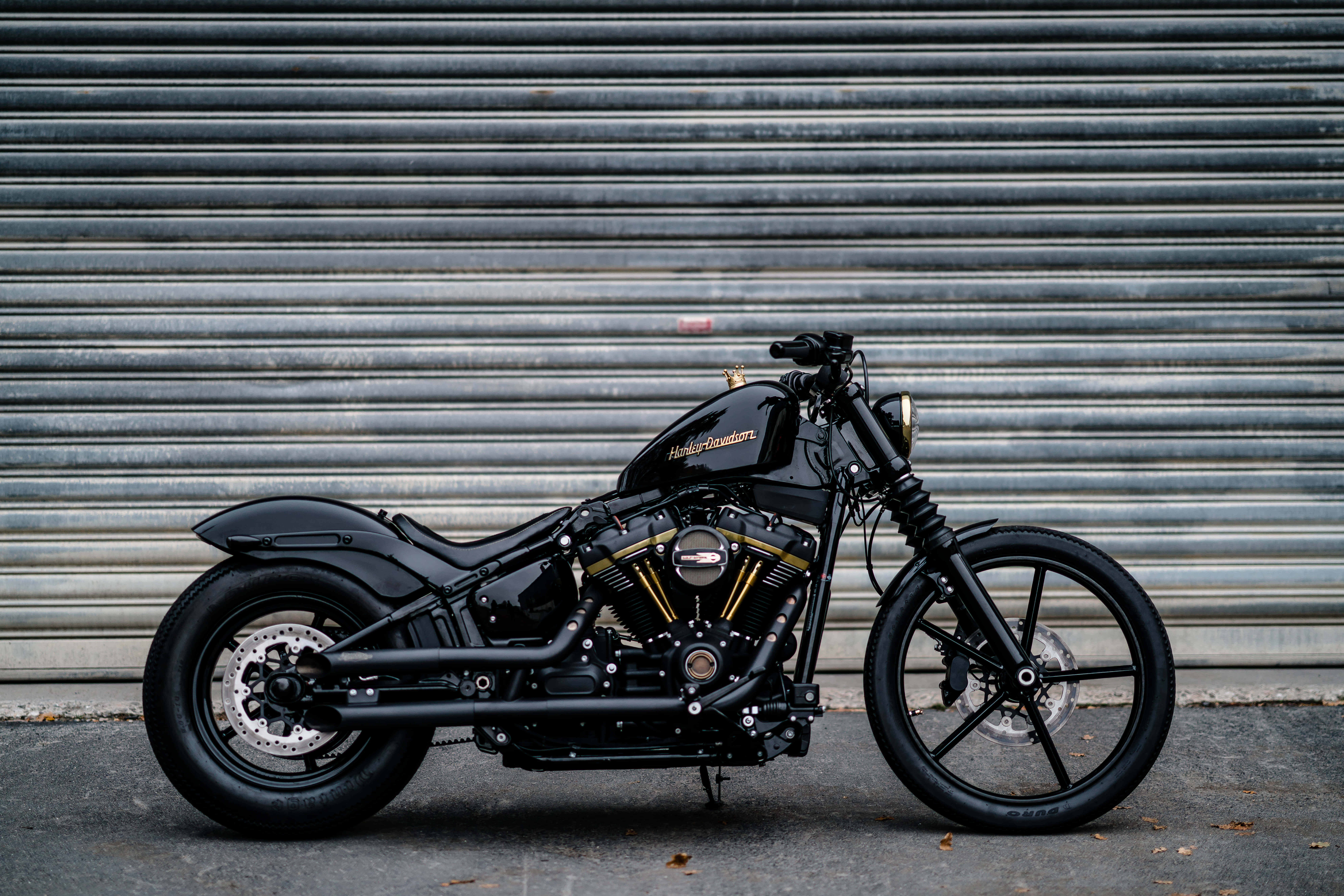 感受騎乘HD摩托車的刺激 壁紙 — 一架型格黑色Harley-Davidson電單車，帶有金色點綴，停泊在波浪形金屬車庫門前。