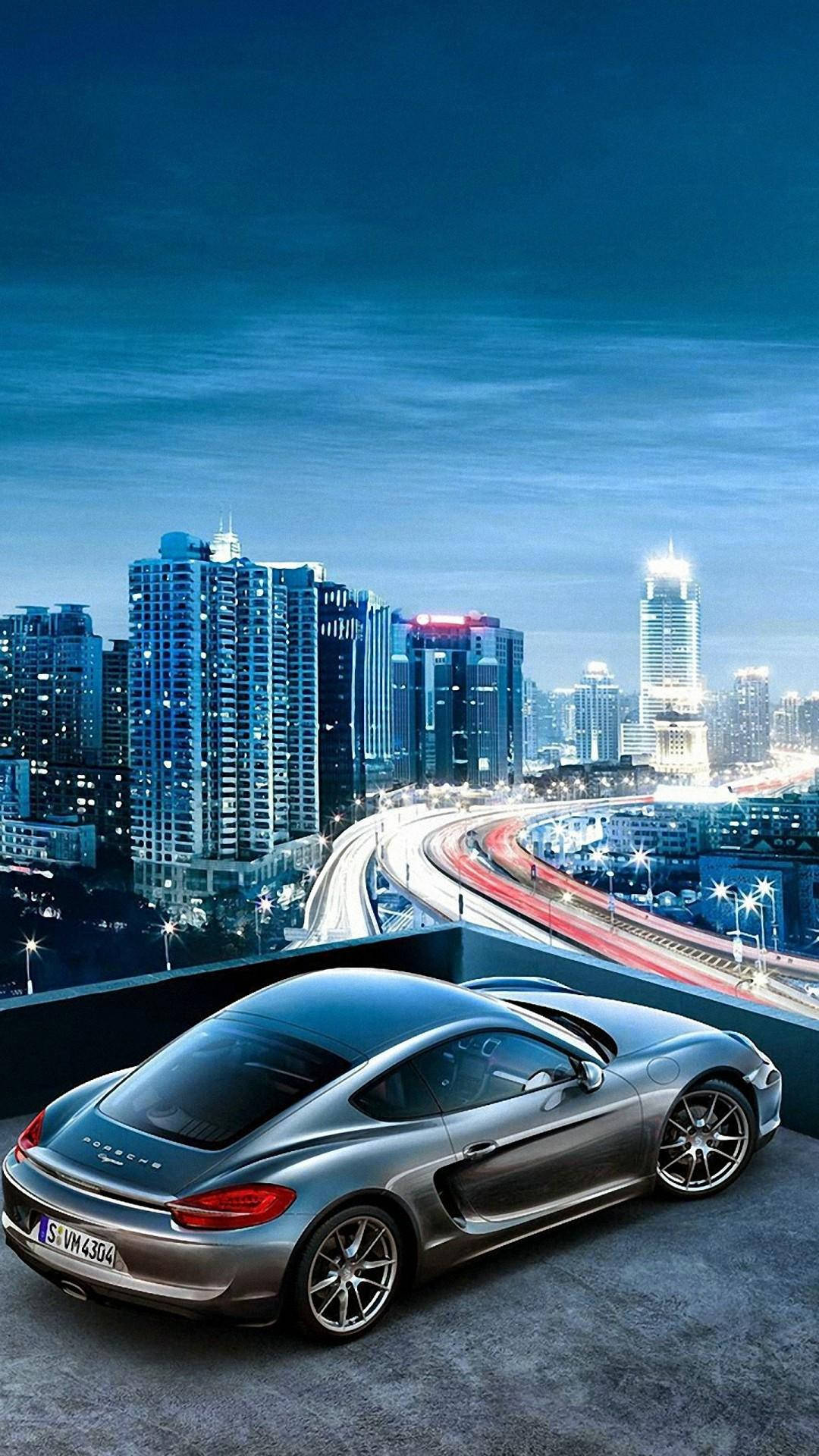 HD 停在城市屋頂的汽車 壁紙 — 一架時尚的銀色跑車停泊在天台上，俯瞰著暮色中充滿活力的城市景觀，伴隨著發光的交通軌跡。