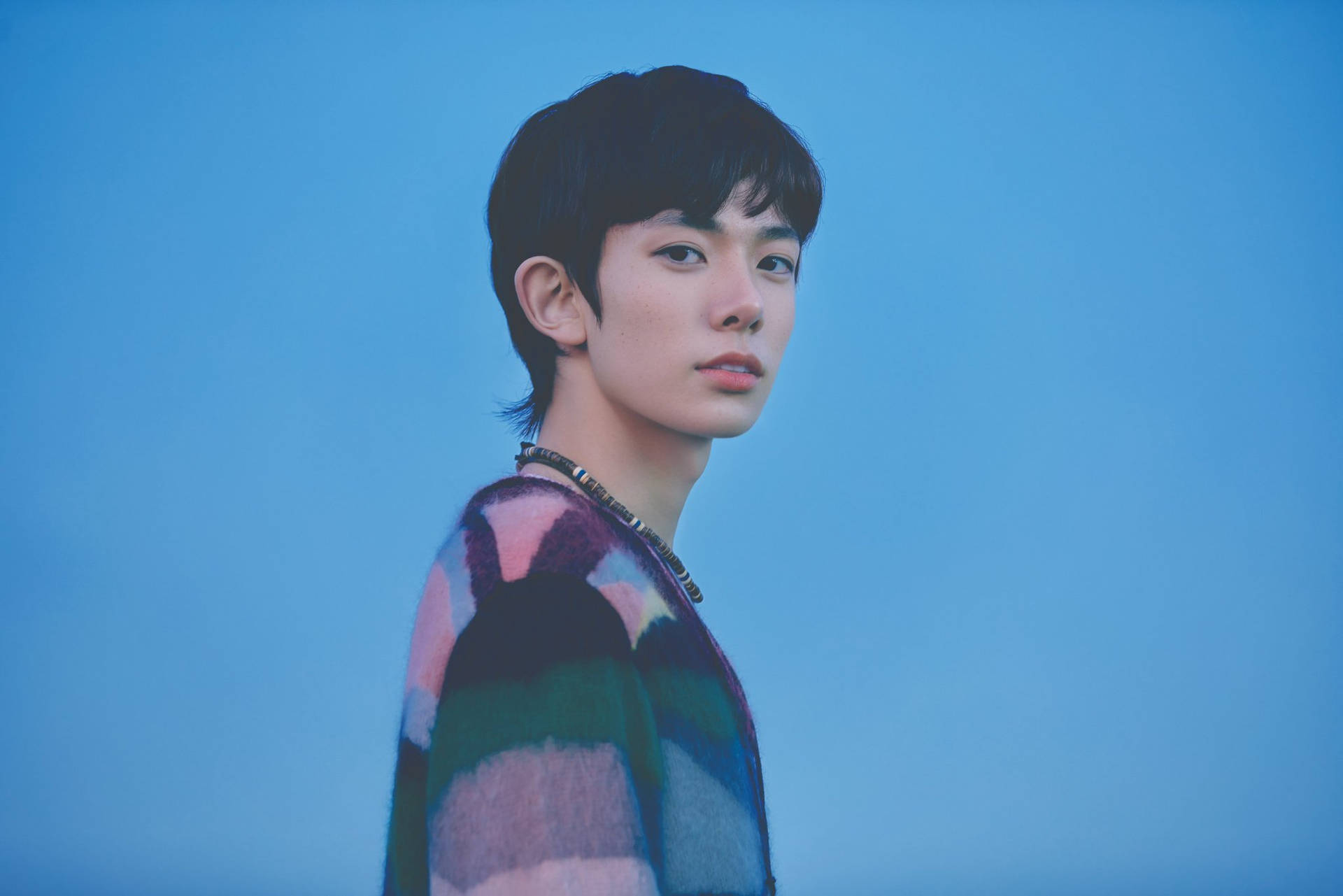 年輕男子穿著彩色毛衣，背景為藍色