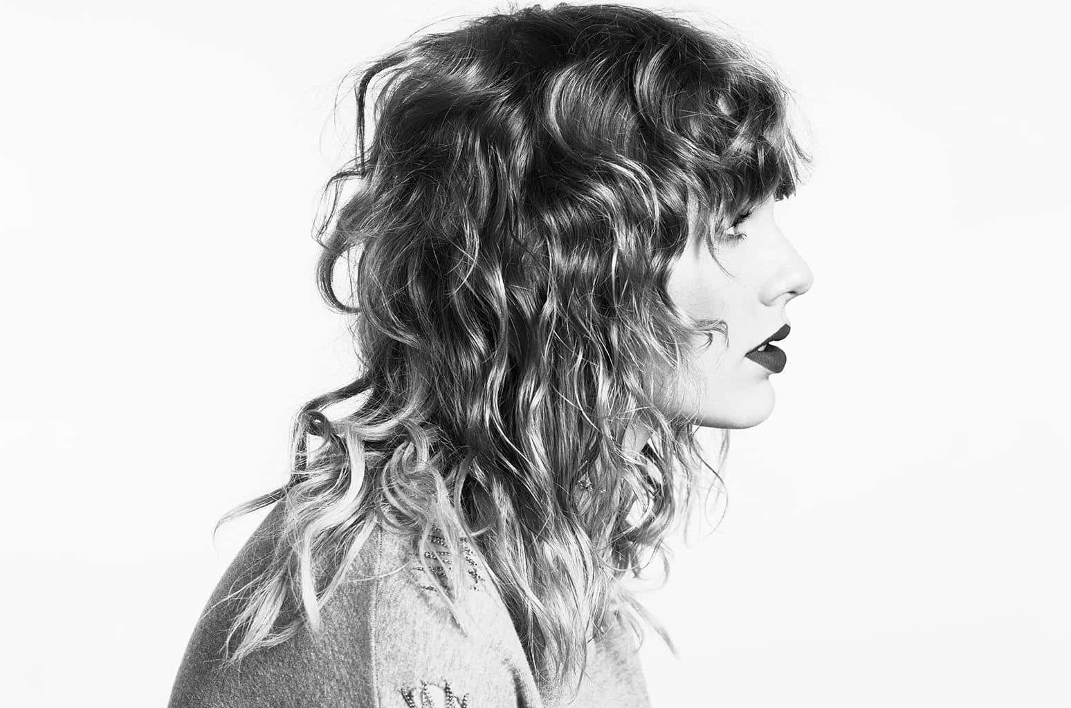 Taylor Swift Lover 桌布 壁紙 — 一個引人注目的黑白肖像，一位擁有豐盈捲髮和大膽嘴唇的女性側面，背景簡潔。