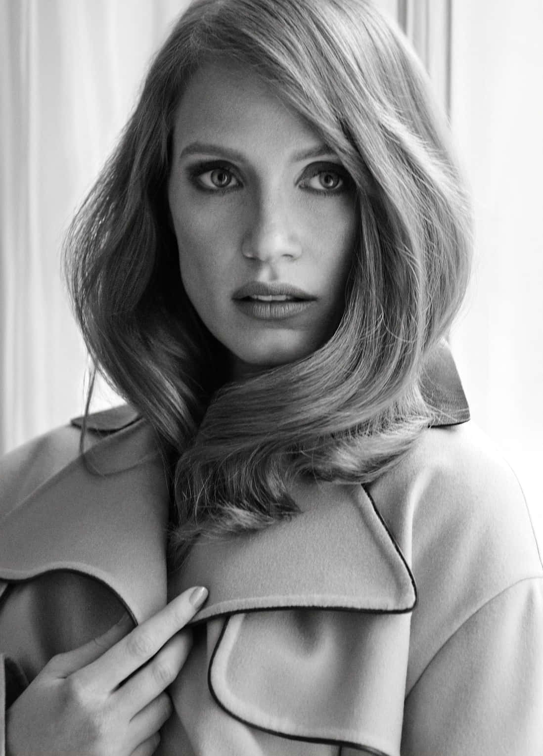 jessica chastain 桌布 壁紙 — 一位波浪髮女性觸摸外套領子直視鏡頭的黑白肖像照。