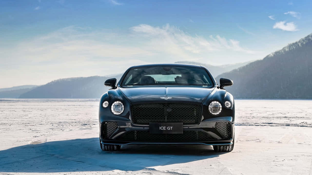 Bentley Continental Gt 桌布 壁紙 — 一輛時尚的黑色Bentley ICE GT停泊在廣闊的雪原上，背景是白雪覆蓋的山脈，天空清澈湛藍。