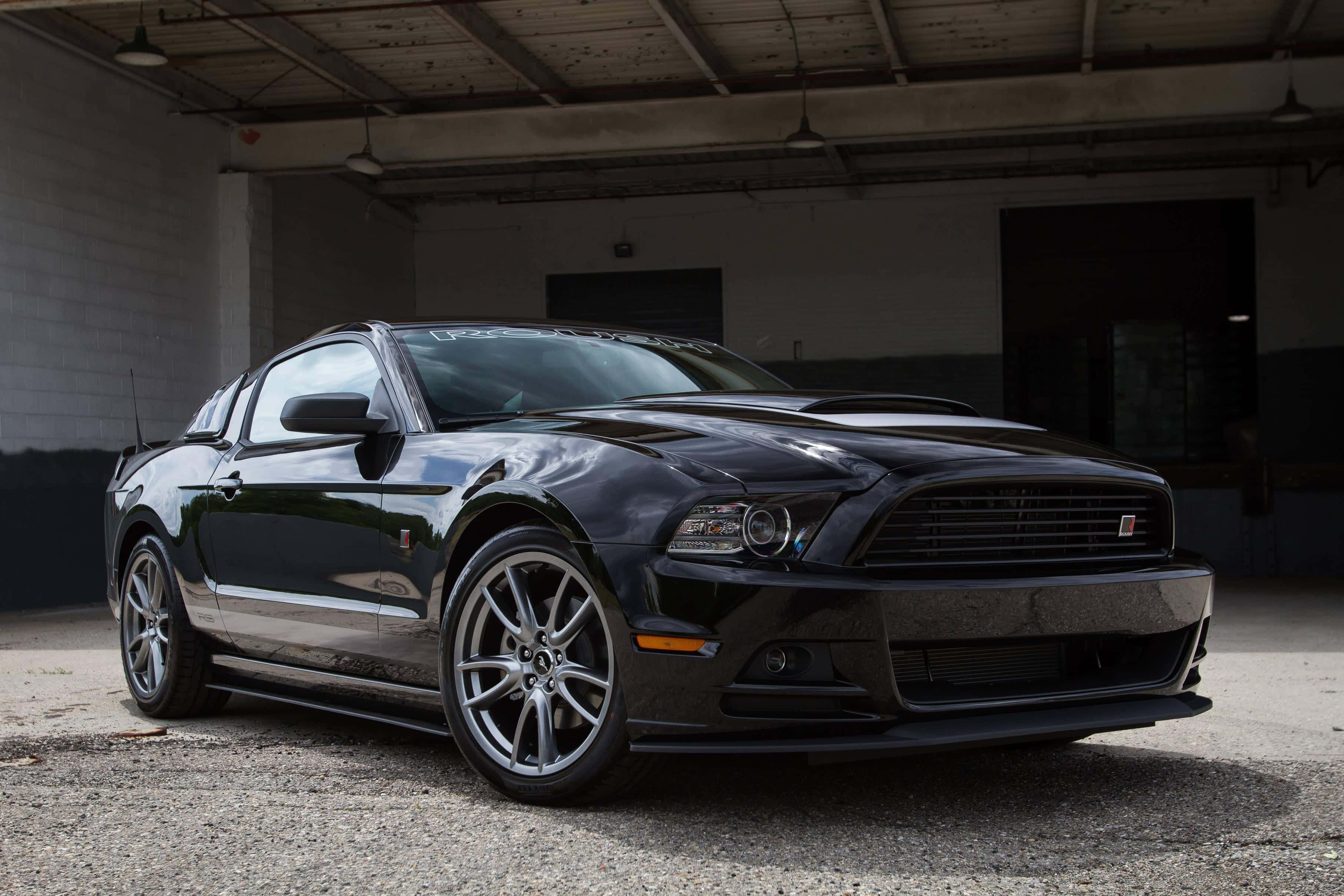 Ford Mustang Roush 桌布 壁紙 — 一架時尚的黑色福特野馬跑車停泊在燈光昏暗的工業車庫內，車庫有混凝土地板和裸露的橫樑。