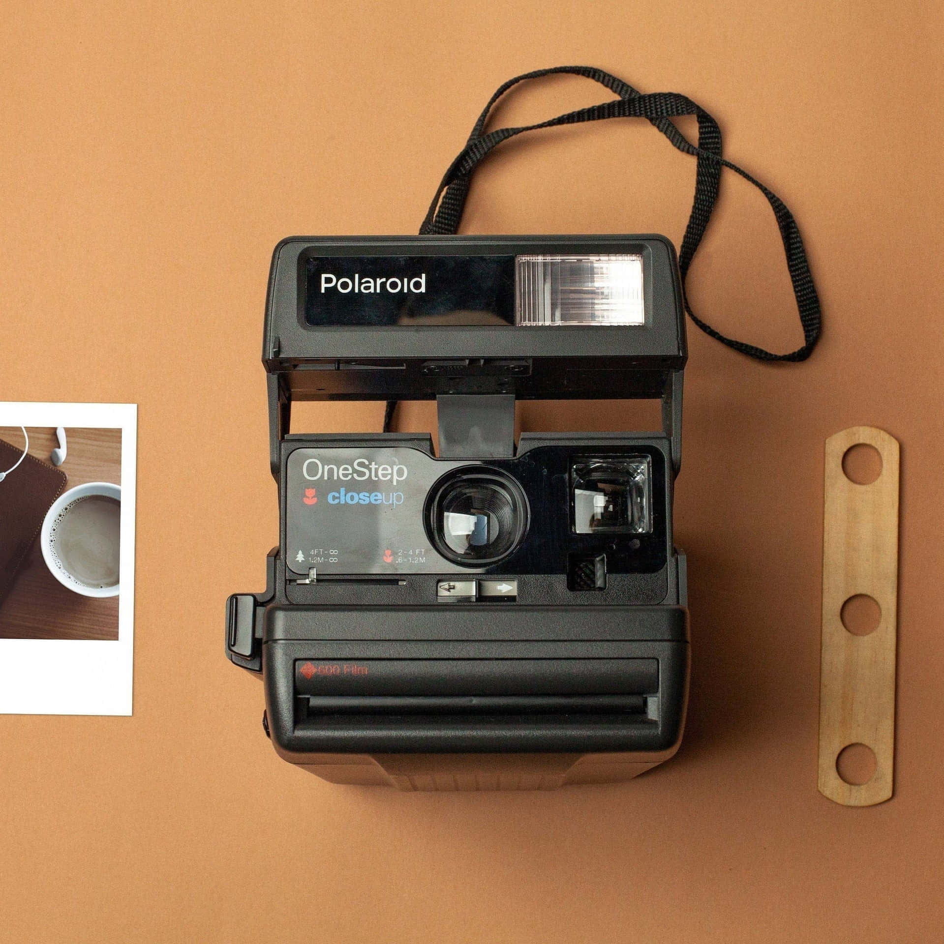  壁紙 — 一部黑色Polaroid OneStep近攝相機放置在溫暖的赤陶表面上，旁邊有一張打印照片和木製工具。