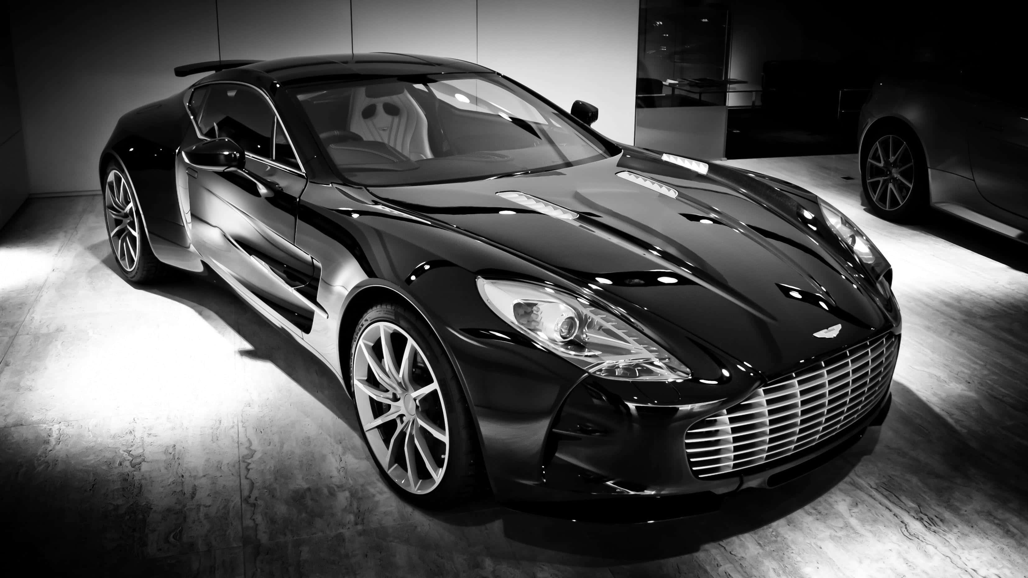 Aston Martin One-77 桌布 壁紙 — 一輛時尚的黑色Aston Martin跑車在極簡主義展廳的戲劇性聚光燈下閃閃發光。