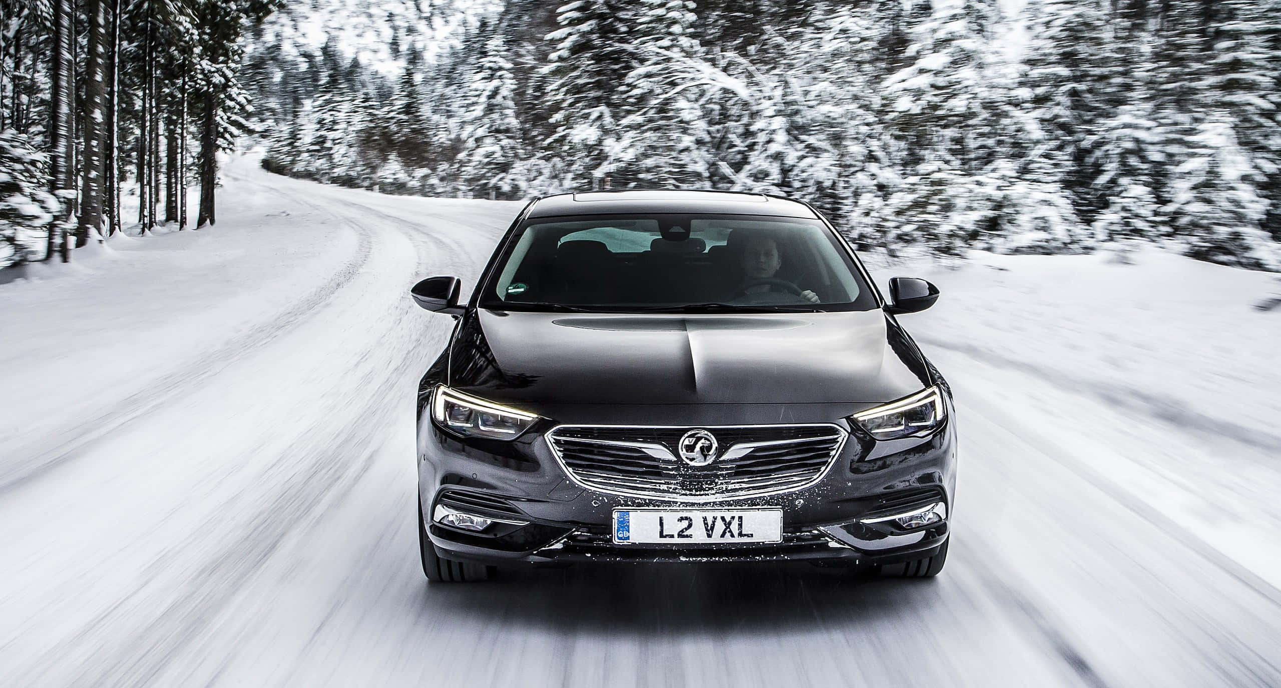 Opel Insignia 桌布 壁紙 — 一輛時尚的黑色豪華轎車在白雪覆蓋的森林道路上飛馳，動態模糊強調其動態運動。