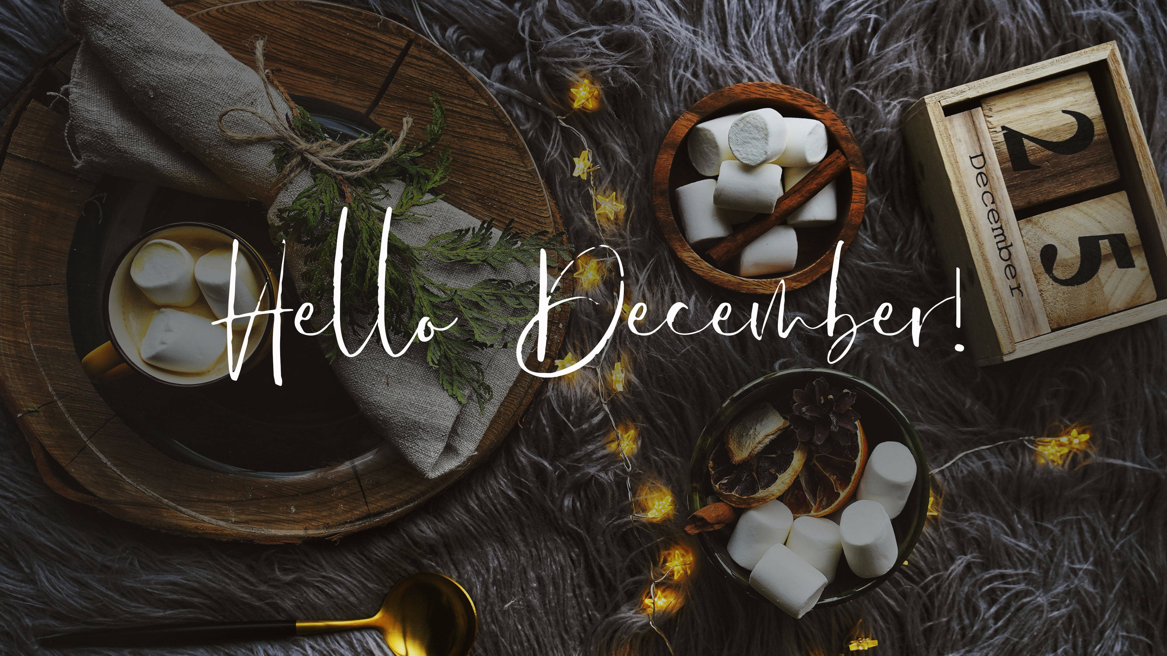Hello December 美學 壁紙 — 舒適的冬季場景，有棉花糖、肉桂棒和木製日曆，放在毛絨灰色地毯上，配上溫暖的仙女燈。