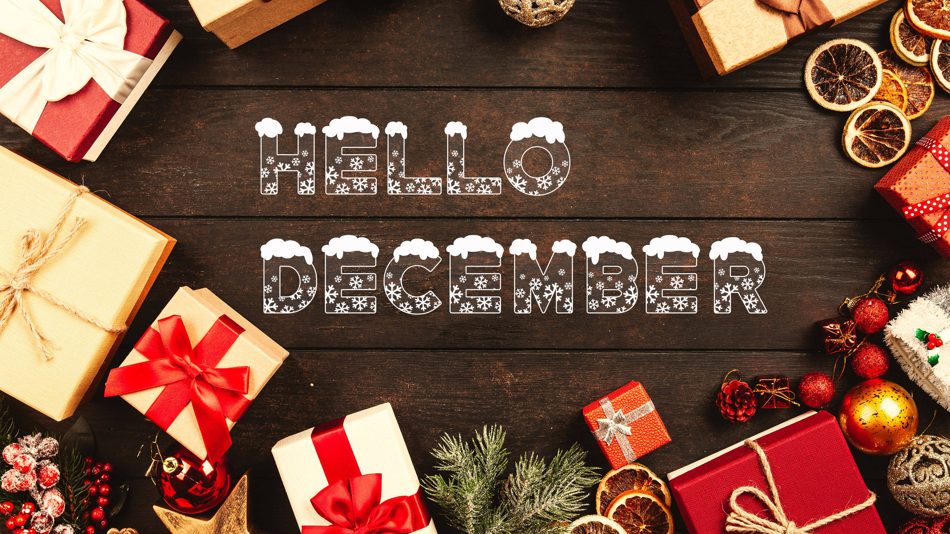 Hello December 聖誕禮物 壁紙 — 深色木桌上擺放著節日紅色、金色和白色的禮物、松枝、乾橙和裝飾品，圍繞著帶有雪花點綴的文字 hello december。