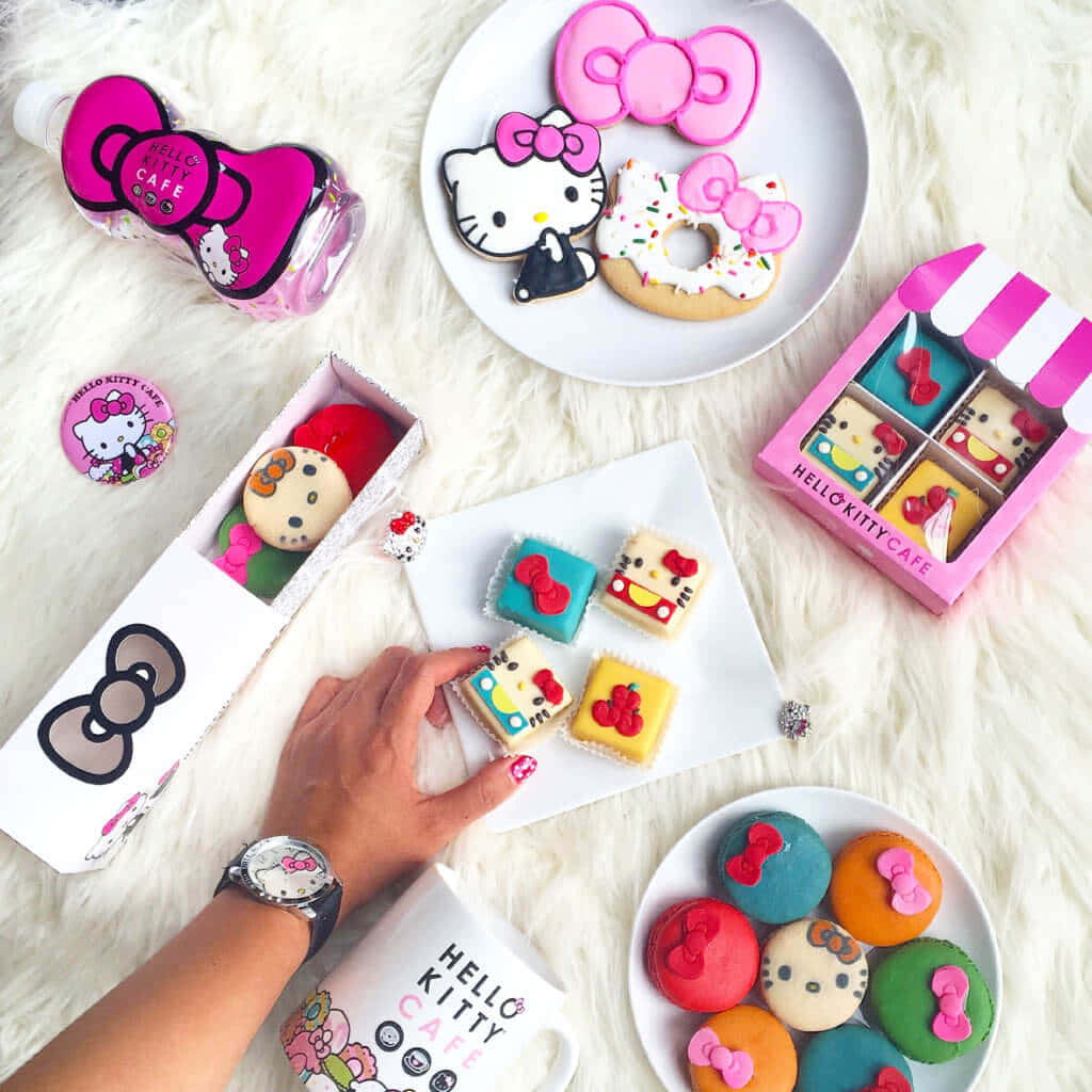 Hello Kitty揮手道別 壁紙 — 一隻手從鋪在毛絨白色地毯上的色彩繽紛主題糕點和商品中拿起一塊Hello Kitty曲奇。
