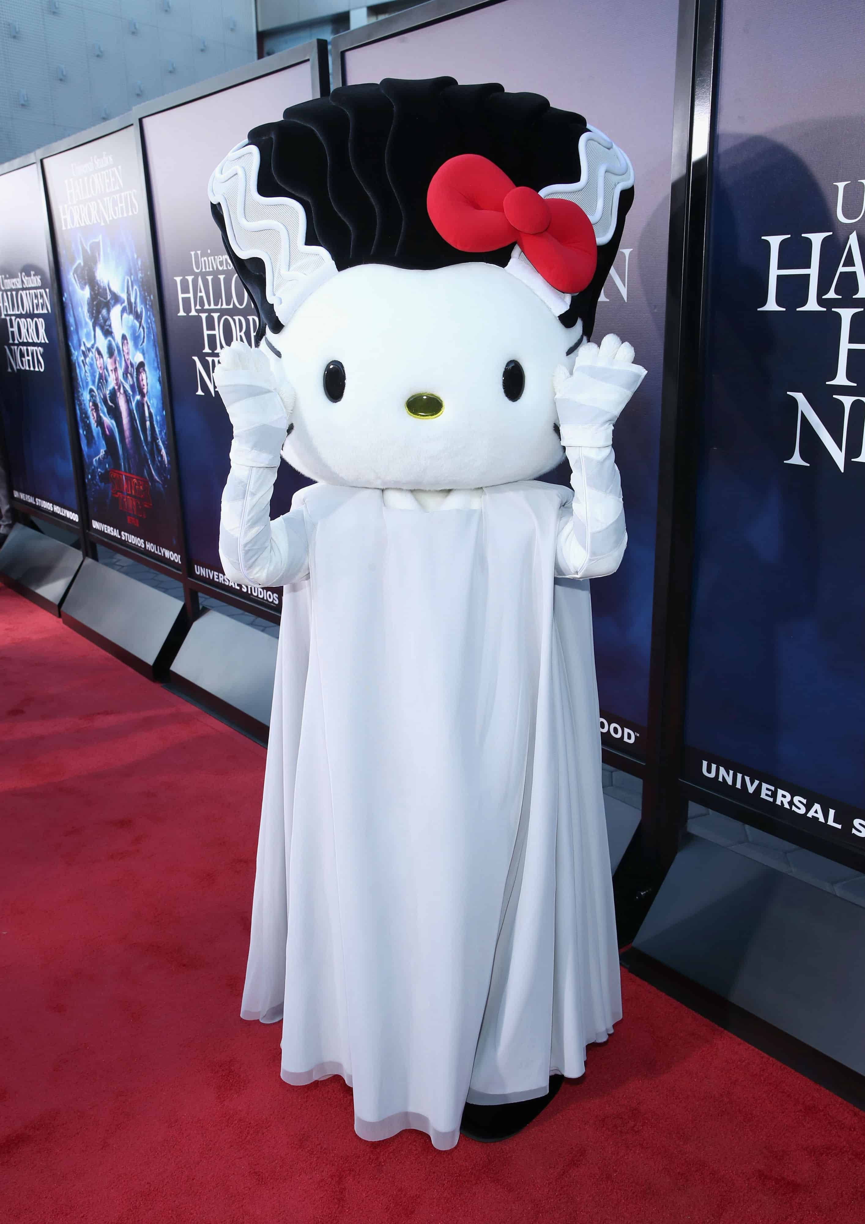 Hello Kitty萬聖節幽靈 壁紙 — Hello Kitty 打扮成鬼魂，戴黑色假髮、紅色蝴蝶結，穿白色長袍，在萬聖節恐怖之夜活動的紅地毯上揮手。