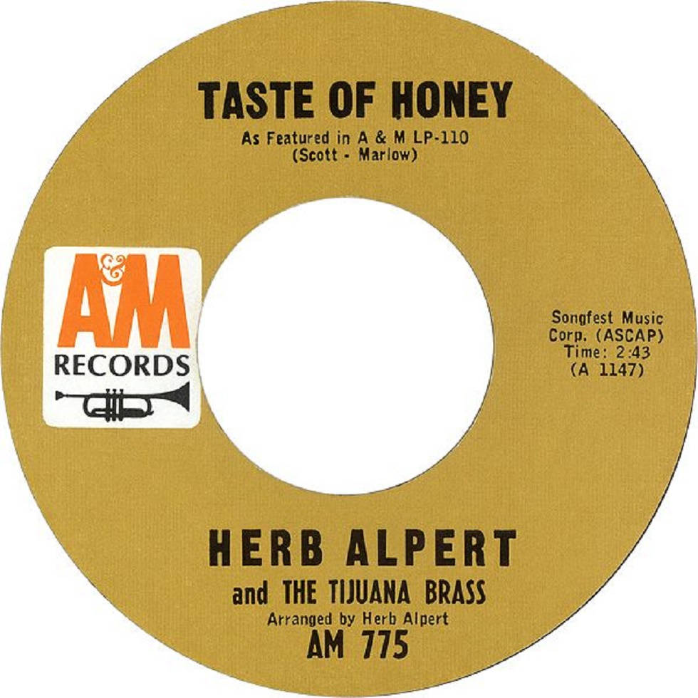 Herb Alpert 帶領 The Tijuana Brass 樂團現場演出 壁紙 — Herb Alpert and The Tijuana Brass 的復古金色黑膠唱片標籤，以粗體黑色文字和 AM Records 標誌呈現「Taste of Honey」。