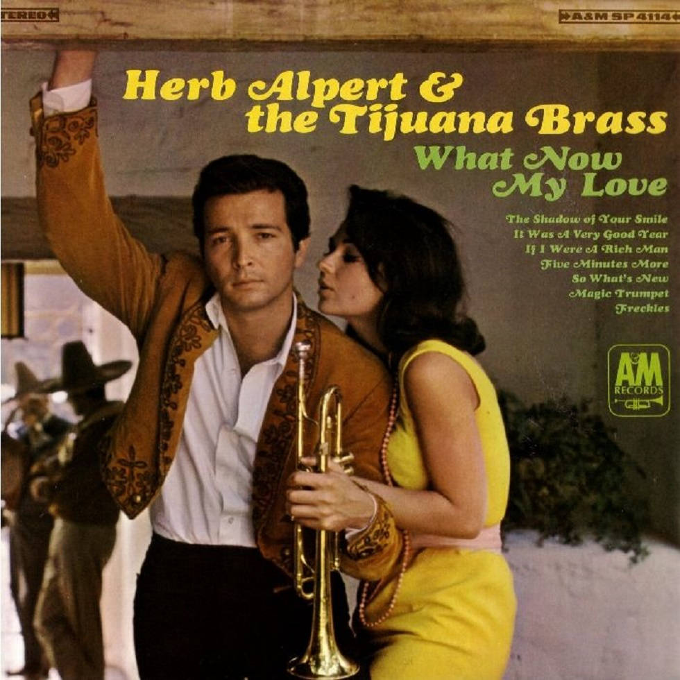 Herb Alpert 與 The Tijuana Brass 專輯封面 壁紙 — 一名身穿棕色刺繡外套的男子和一名身穿黃色連衣裙的女子在質樸的木質背景下拿著小號擺姿勢。