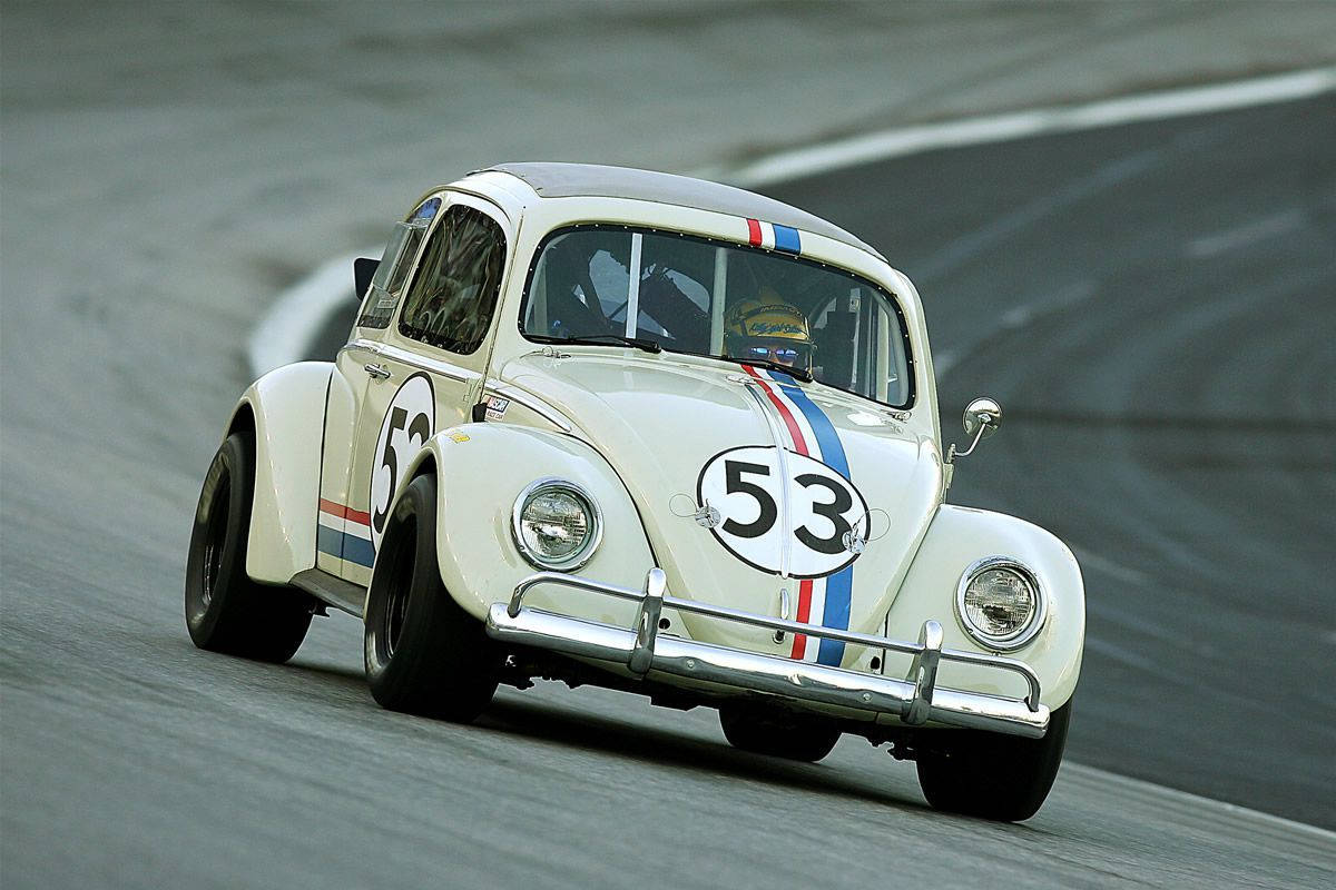 《Herbie：Fully Loaded》賽道駕駛壁紙 壁紙 — 一輛白色賽車改裝福士甲蟲車，編號53，在灰色瀝青賽道上飛馳。