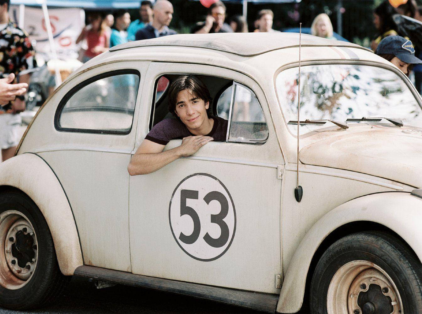 《Herbie Fully Loaded》賈斯汀·朗 壁紙 — 一名年輕男子在熱鬧的戶外活動中，從一輛帶有53號的復古白色賽車的窗戶探出身子。