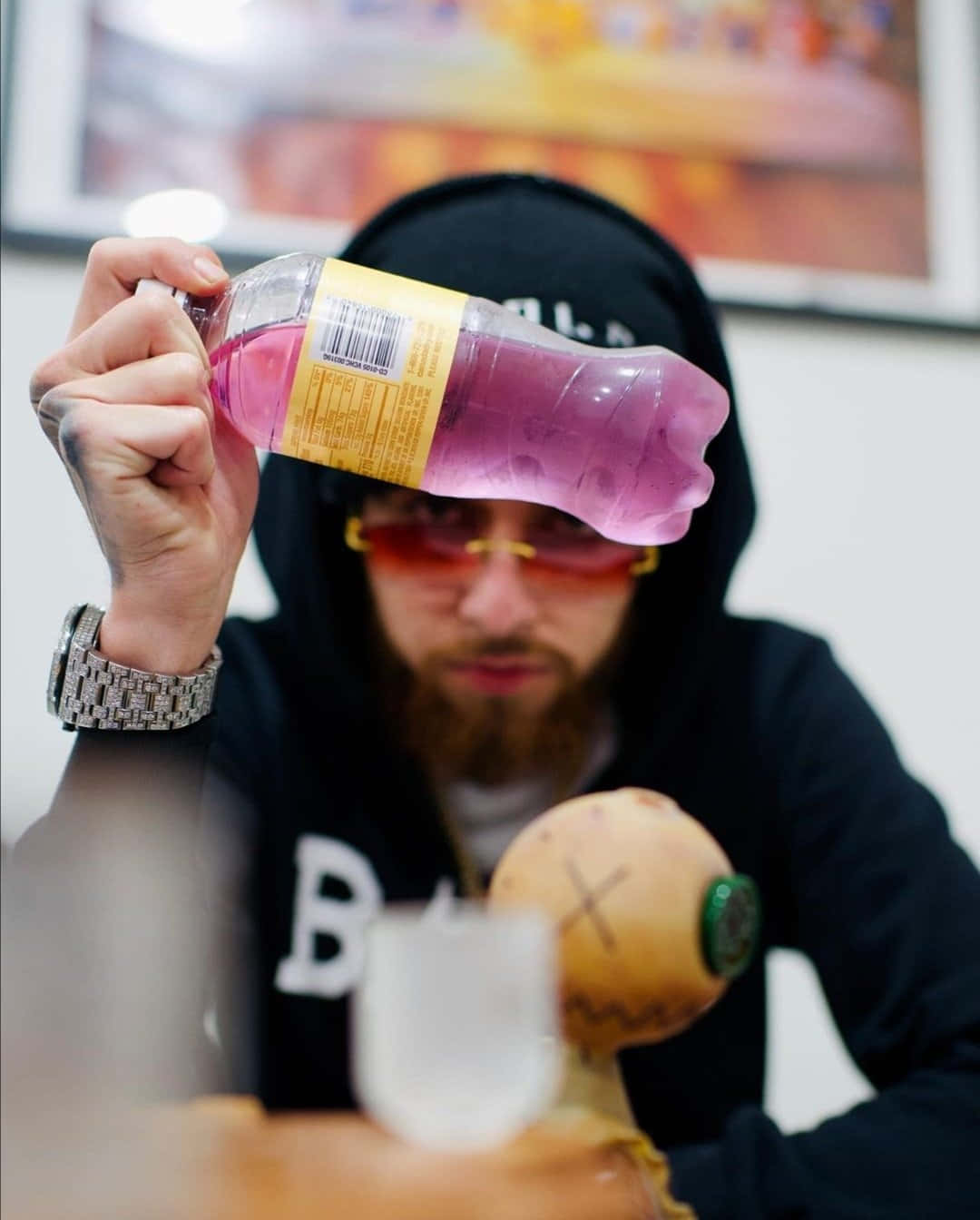 戴著太陽眼鏡和連帽衫的男人將粉紅色飲料瓶舉在眼前。