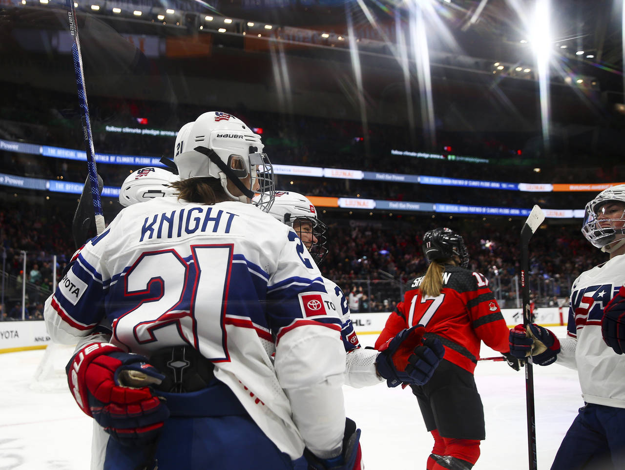 Hilary Knight 奧運金牌得主 壁紙 — 美國女子冰球運動員在明亮的場館燈光下，以人群為背景，在冰上慶祝入球。
