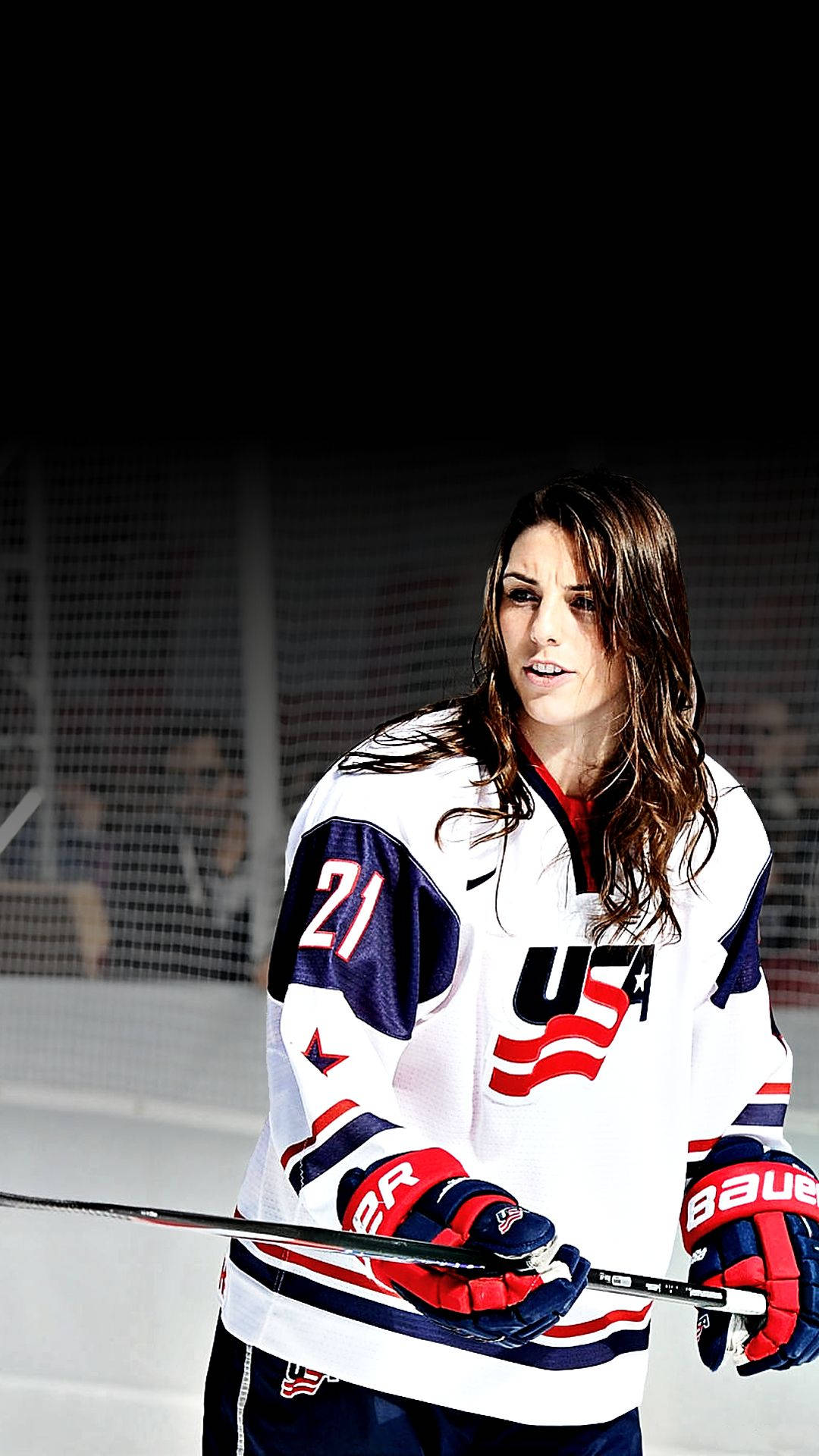 Hilary Knight 星級前鋒賽場英姿 壁紙 — 一位專注的女冰球運動員身穿美國隊球衣，在明亮的場館燈光下於冰場上握著球桿。
