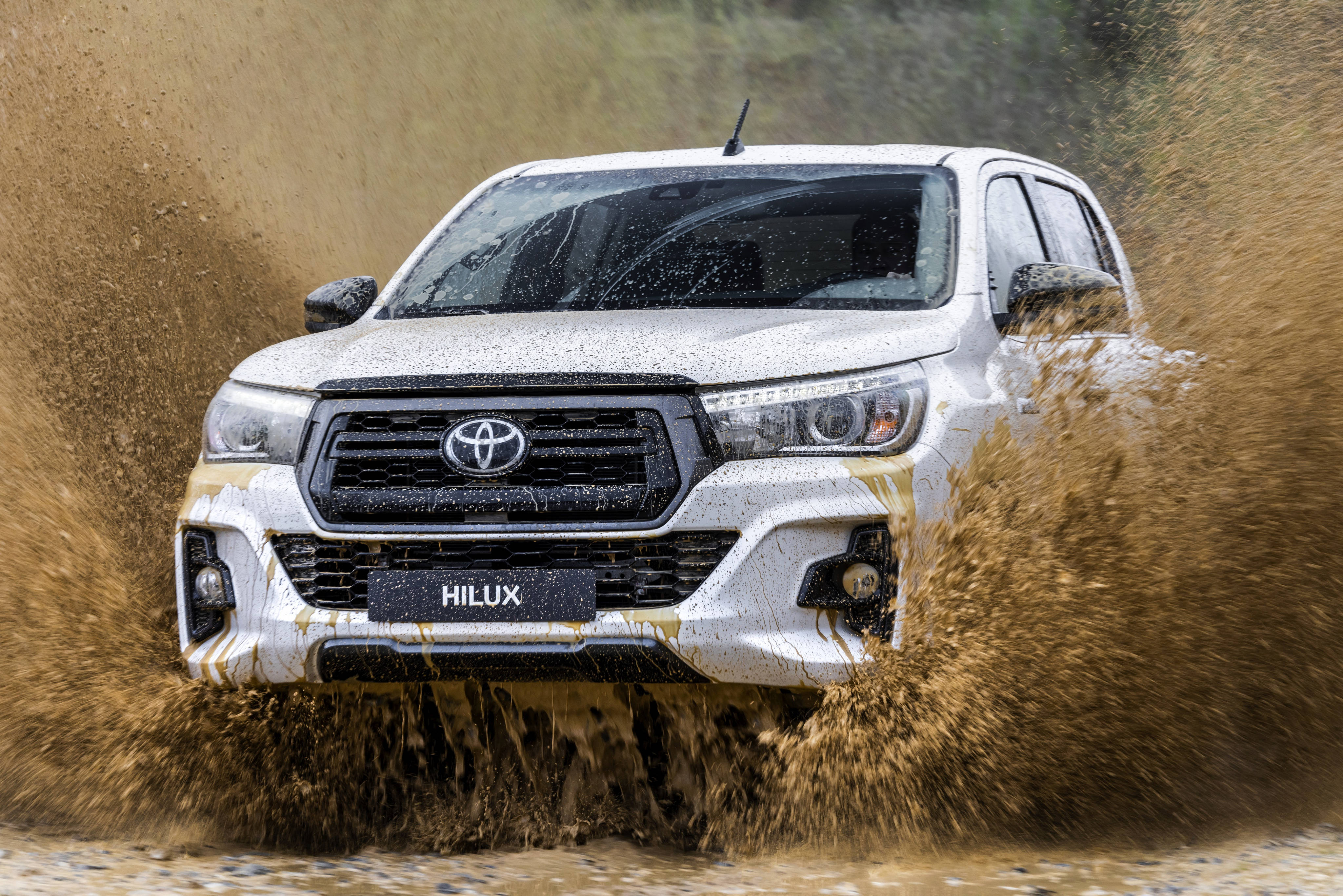 涉水豐田 Hilux 4K 壁紙 — 一輛白色豐田 Hilux 貨車駛過泥水，車頭格柵周圍濺起棕色水花。