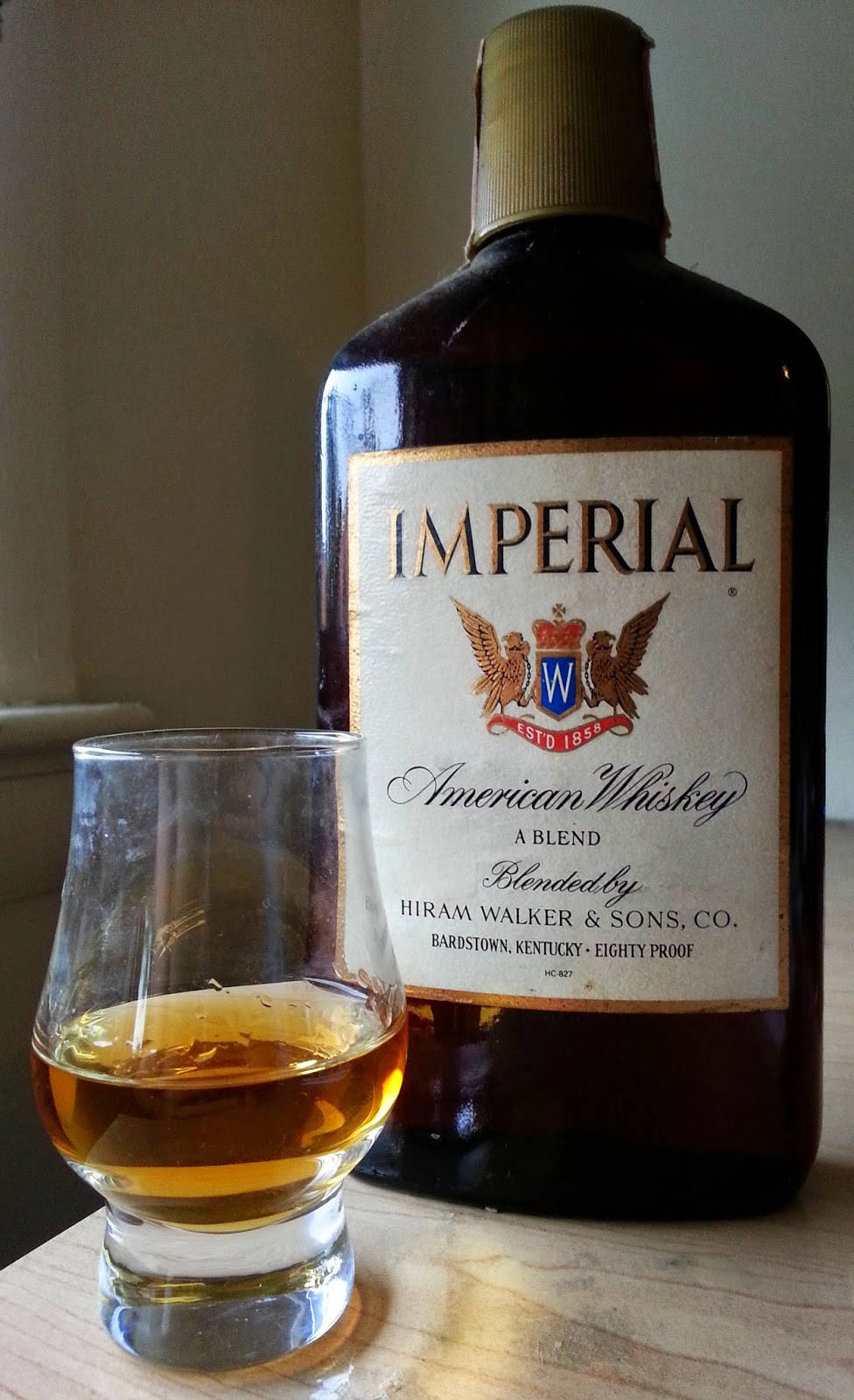 Hiram Walker 帝國美國威士忌 壁紙 — 一瓶Imperial American Whiskey和一杯琥珀色液體放在木質表面上，室內光線柔和。