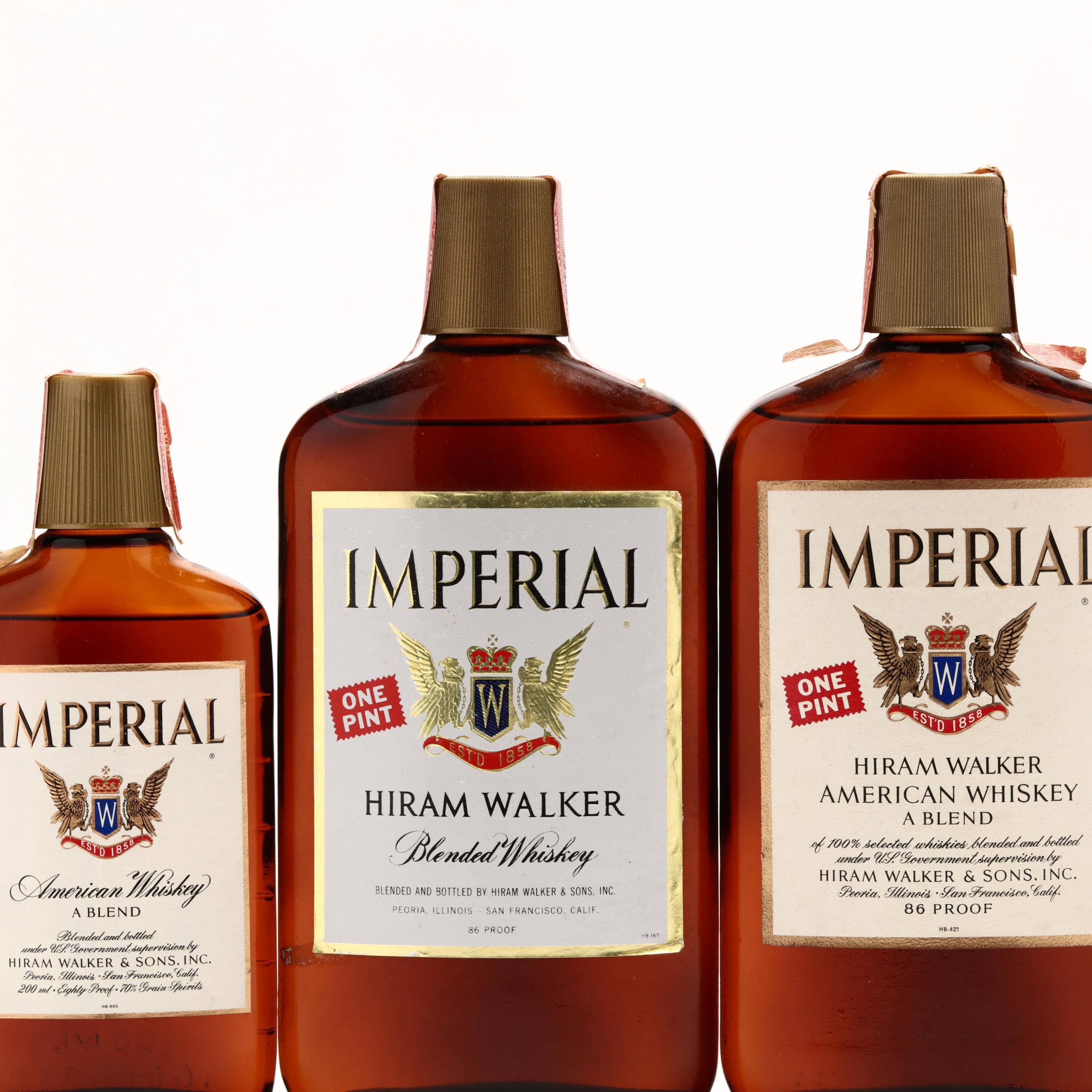 Hiram Walker & Sons 美國威士忌混合款 壁紙 — 三瓶琥珀色玻璃瓶裝 Imperial American Whiskey，配有金色瓶蓋和復古標籤，在純白背景前整齊排列。