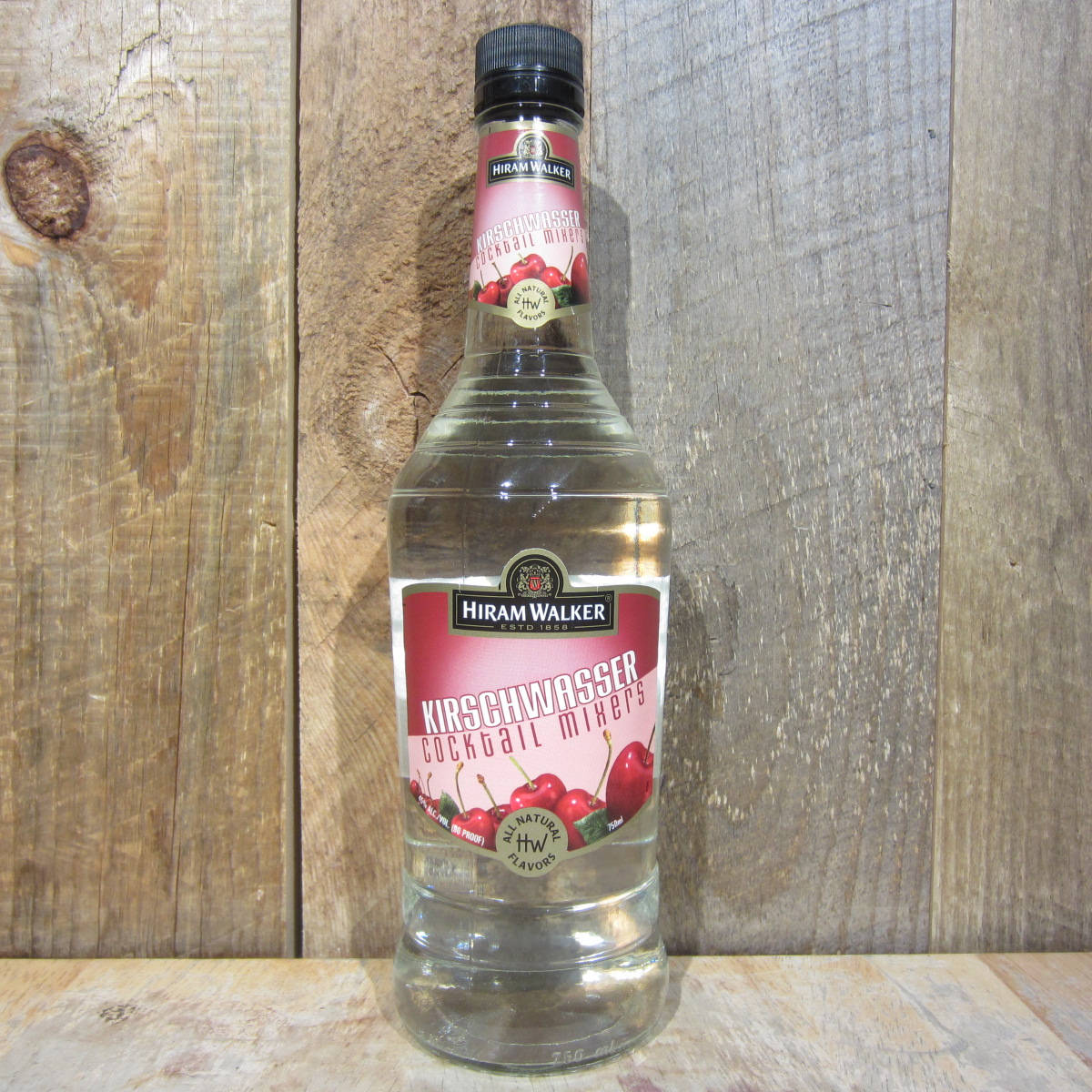 Hiram Walker 樱桃利口酒瓶 壁紙 — 一瓶透明的Hiram Walker Kirschwasser雞尾酒調和器，帶有櫻桃圖案，立在質樸的木質背景前。