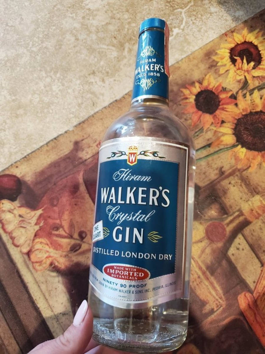 Hiram Walker 水晶金酒瓶 壁紙 — 一隻手拿著一瓶透明的 Hiram Walker's Crystal Gin 琴酒，背景是向日葵圖案。