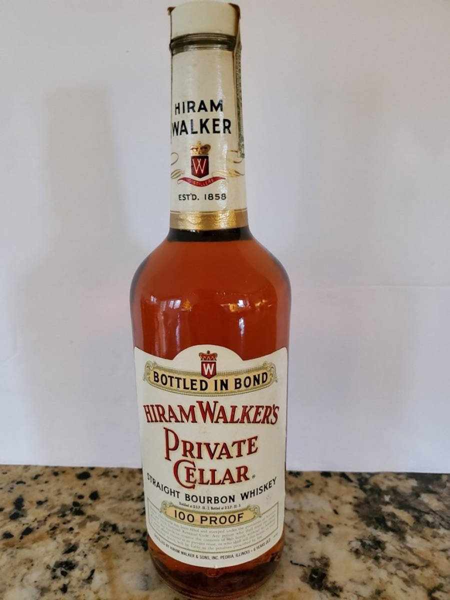Hiram Walker 私人酒窖直火波本威士忌 壁紙 — 一瓶Hiram Walker's Private Cellar 100 proof straight bourbon威士忌放在有斑點的枱面上，背景是純白色的牆壁。