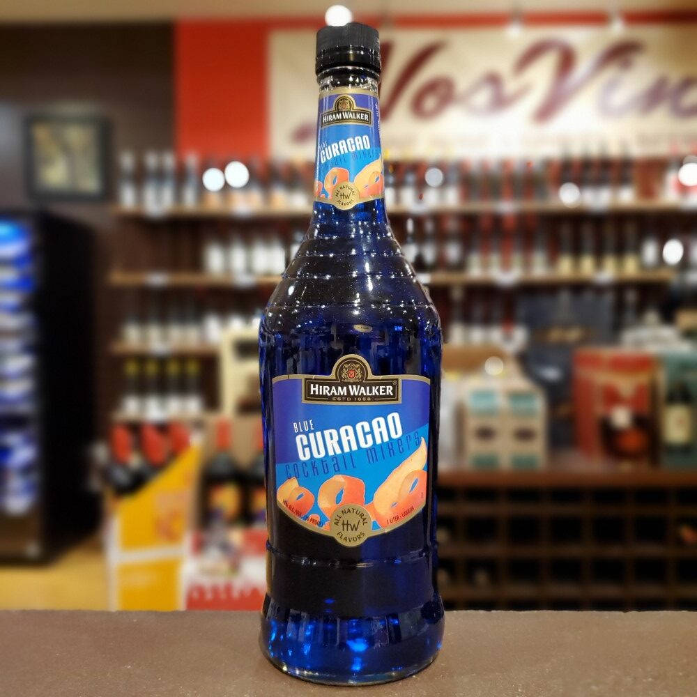 Hiram Walker 藍橙力娇酒調酒配料整齊陳列 壁紙 — 一瓶鮮藍色的Hiram Walker Blue Curacao雞尾酒調和劑醒目地放在吧檯上，背景是模糊的酒架。
