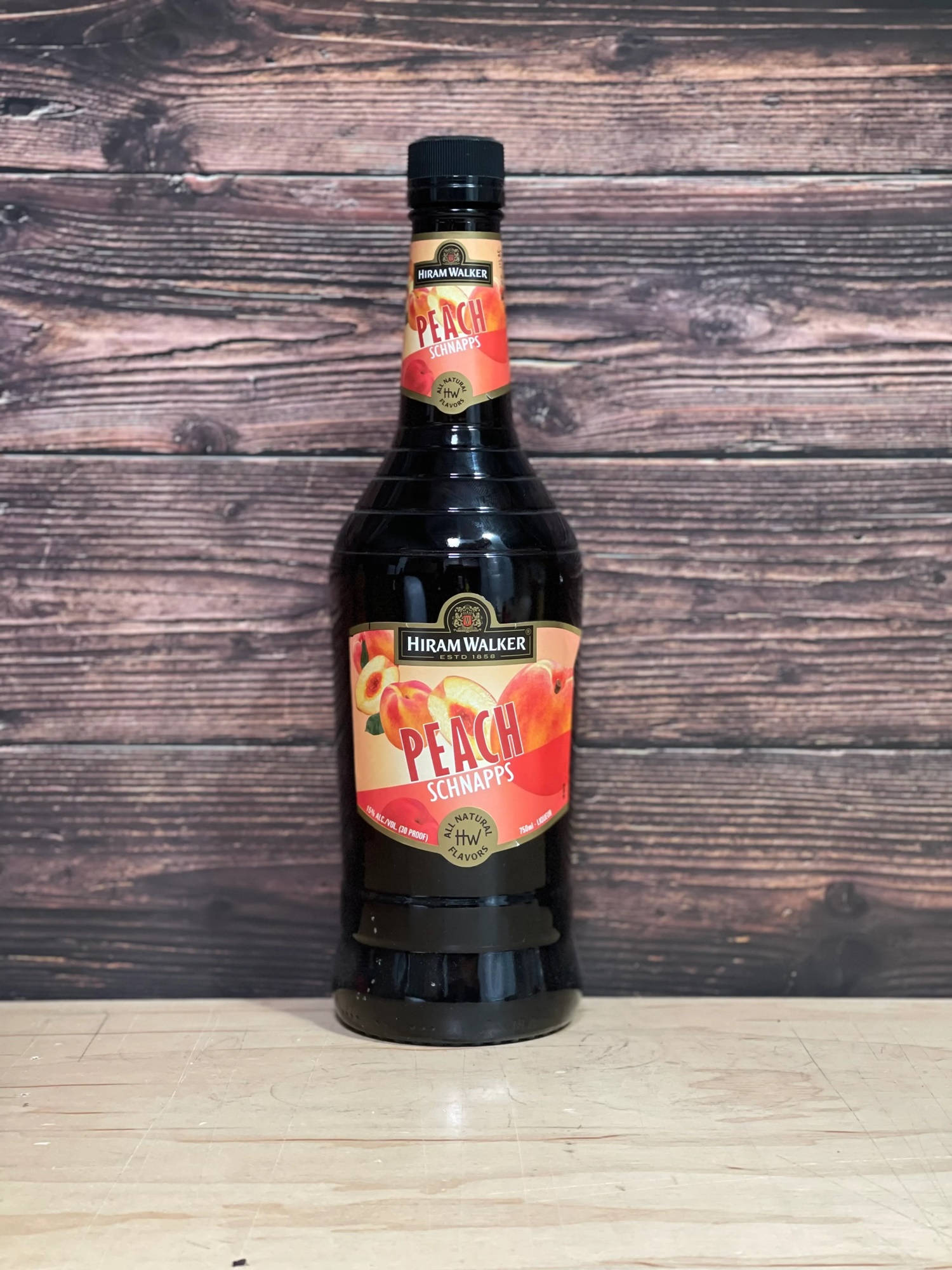 Hiram Walker 蜂蜜桃子風味利口酒瓶攝影 壁紙 — 一瓶Hiram Walker Peach Schnapps放在淺色木質表面上，背景是深色質樸的木質背景。