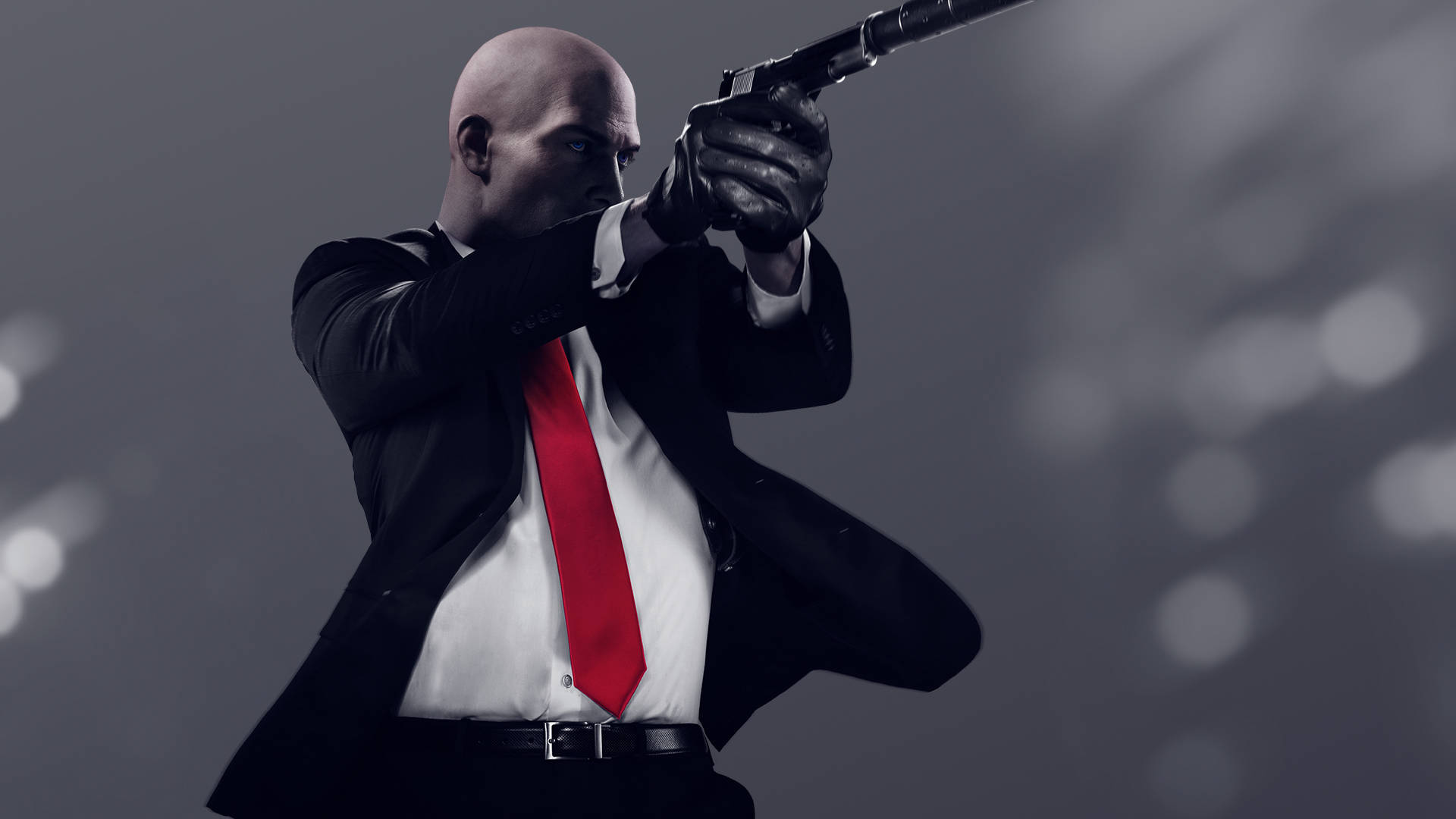 《Hitman 2018》特工47持槍瞄準 壁紙 — 一個光頭男人穿著黑色西裝和紅色領帶，在模糊的灰色背景下，專注地瞄準一把左輪手槍。