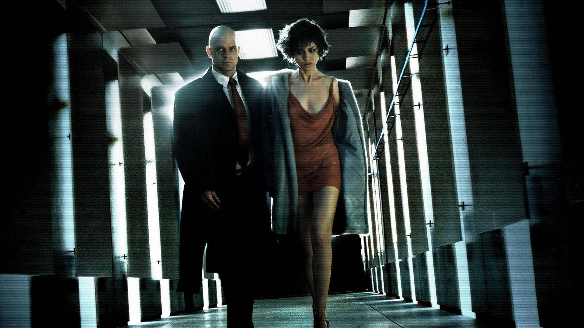 《Hitman Absolution》特工47角色扮演 壁紙 — 兩個身影走在一條光線刺眼的螢光燈走廊上，重複的幾何面板投下戲劇性的陰影。