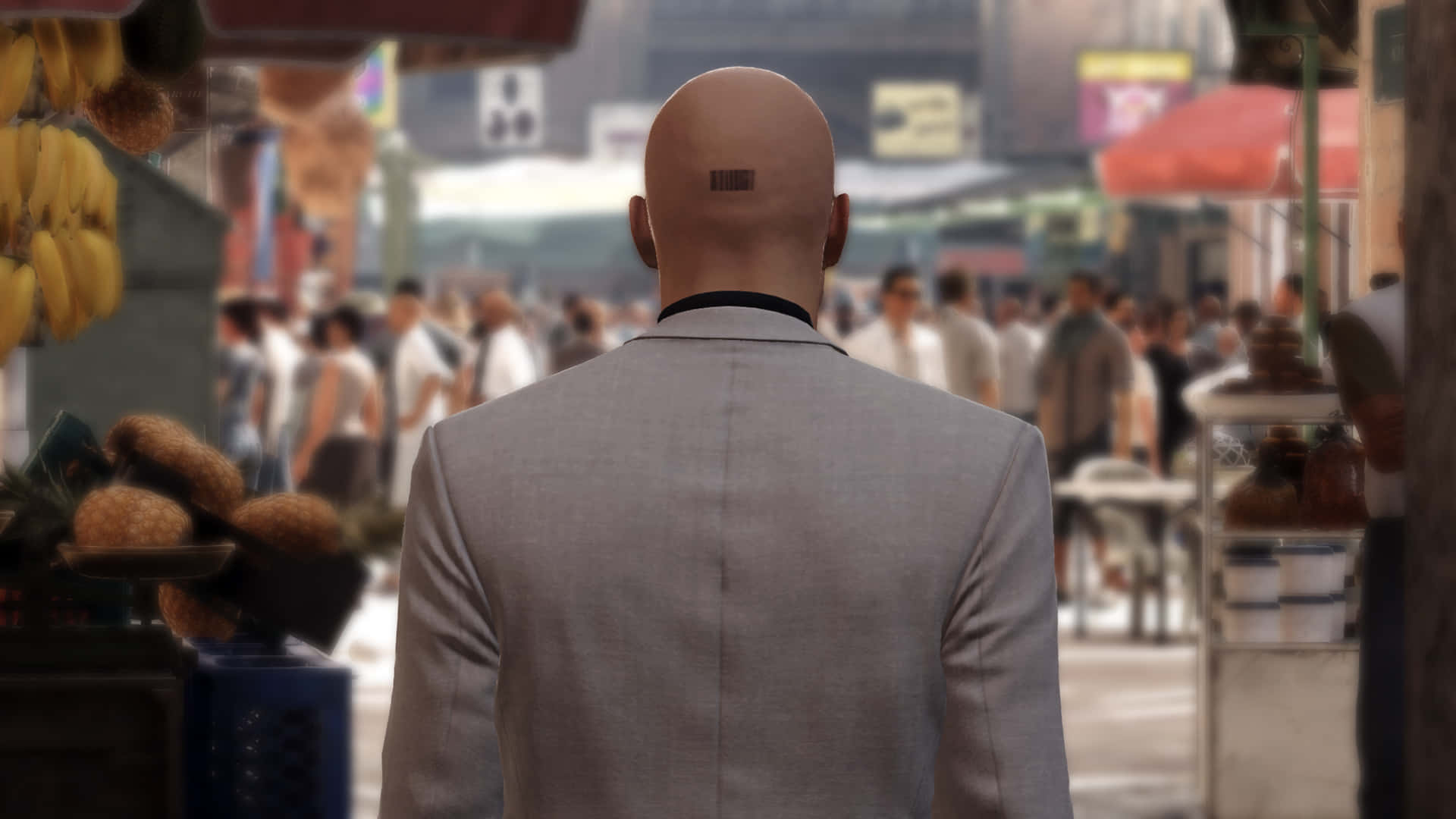 《Hitman》系列中Agent 47的銀色手槍特寫 壁紙 — 一個光頭男人穿著灰色西裝，沿著一條擺滿水果攤和人群的繁華城市街道走開。