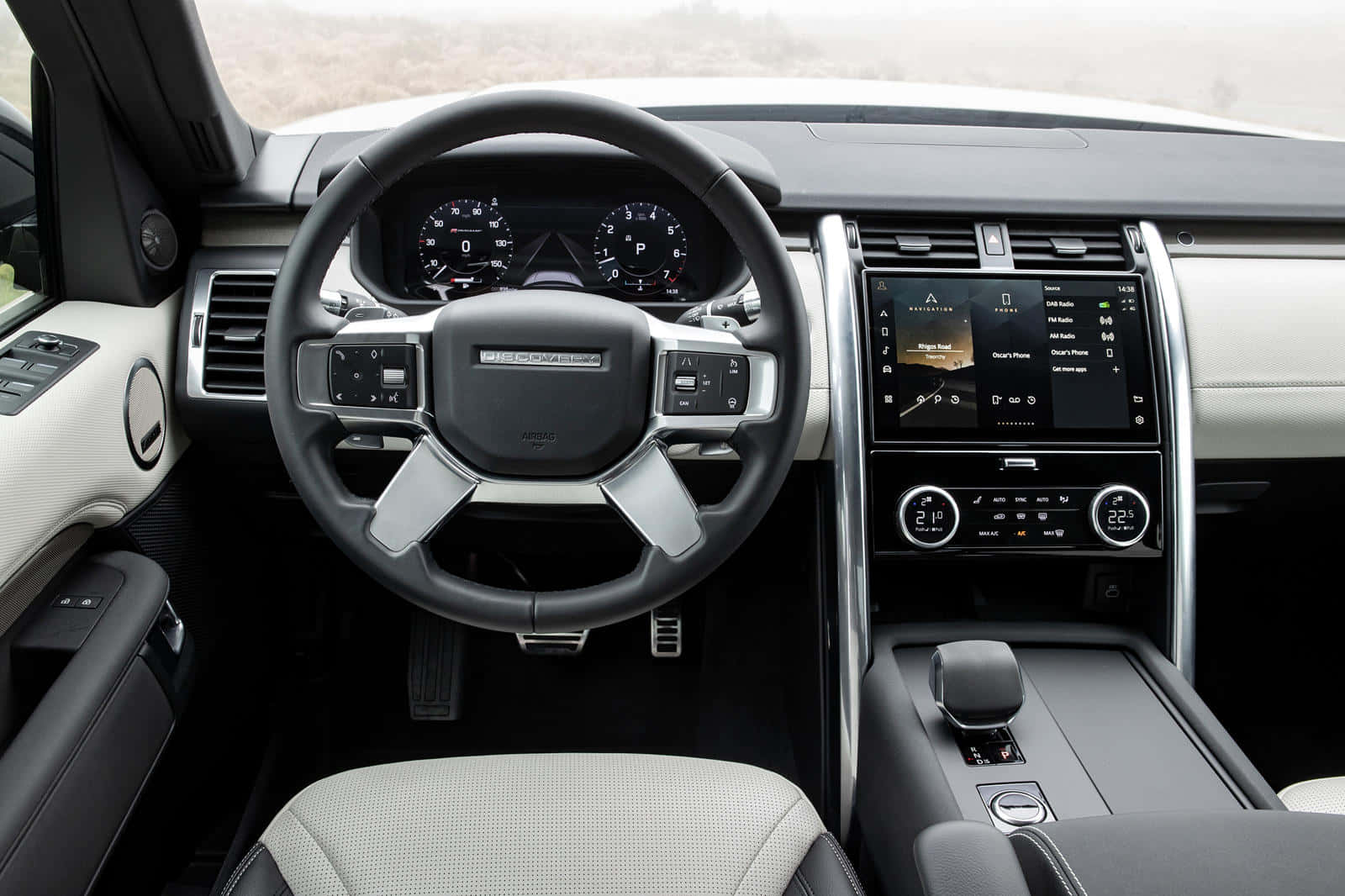 Land Rover Discovery 桌布 壁紙 — 豪華SUV內飾，黑色方向盤配銀色飾邊，數碼儀表板顯示車輛控制和空調設定。