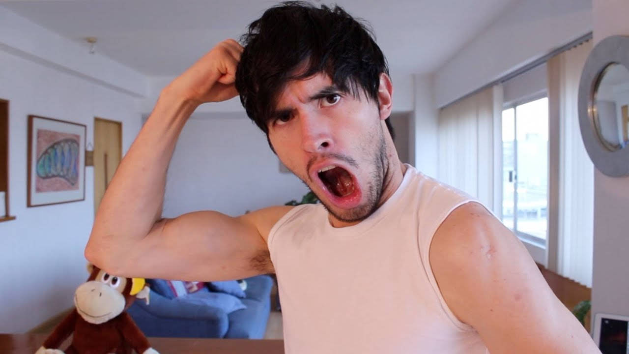 HolaSoyGerman 展示肌肉 壁紙 — 一名深色頭髮和鬍鬚的男人在光線明亮的客廳中彎曲二頭肌並尖叫。