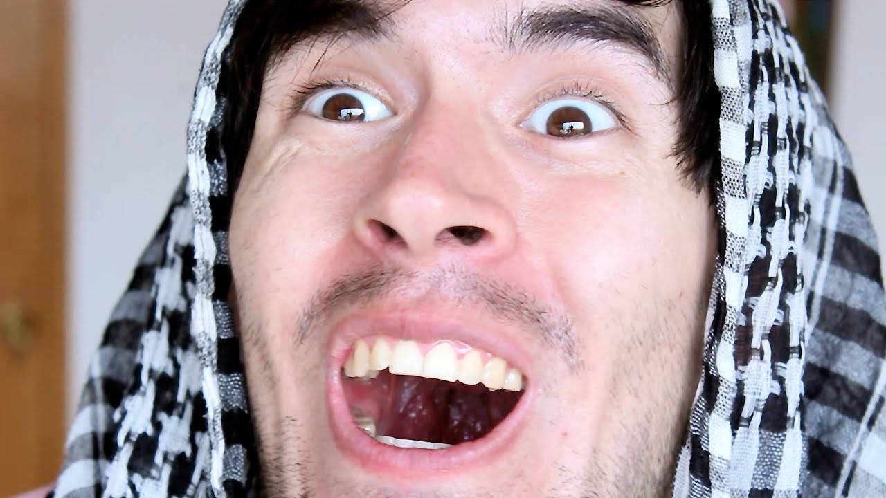HolaSoyGerman 幽默表情特寫 壁紙 — 一個戴著黑白格仔頭巾嘅男人，喺特寫鏡頭中瞪大雙眼、張開嘴巴凝視。