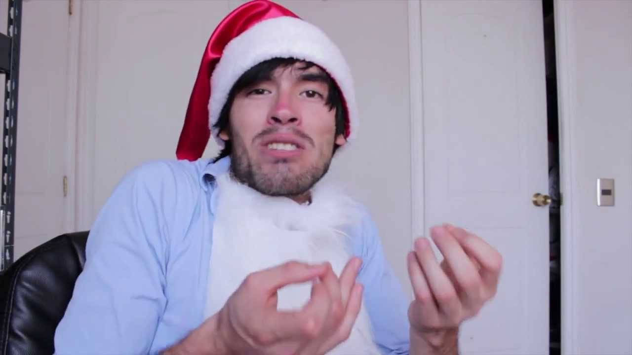 HolaSoyGerman 戴聖誕帽 壁紙 — 一名戴著聖誕帽、留著白鬍子的男子，在室內靠著素牆坐著，生動地做著手勢。