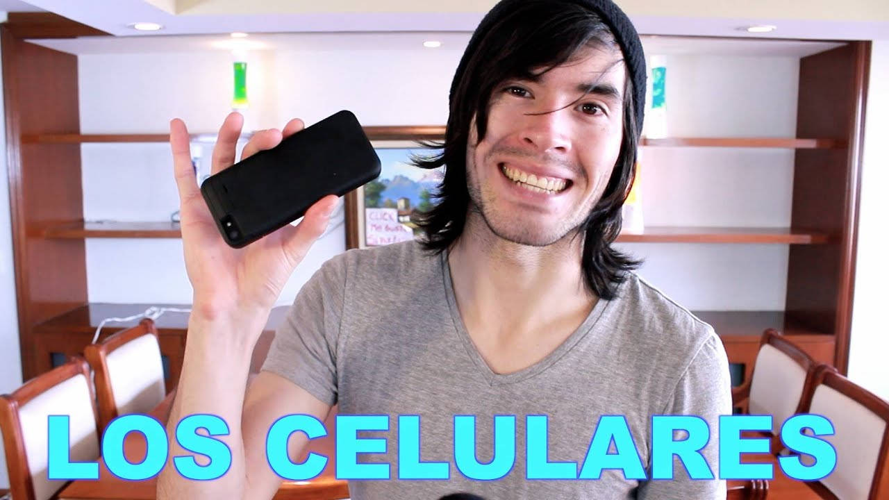 HolaSoyGerman「手機」影片封面 壁紙 — 一位微笑的長黑髮男士在溫暖照明的室內環境中舉起一部黑色智能手機。