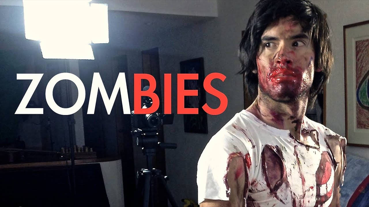 HolaSoyGerman 扮演殭屍 壁紙 — 一個穿著血淋淋喪屍服裝的人站在一個有照明設備的攝影棚中，並疊加了「zombies」字樣。