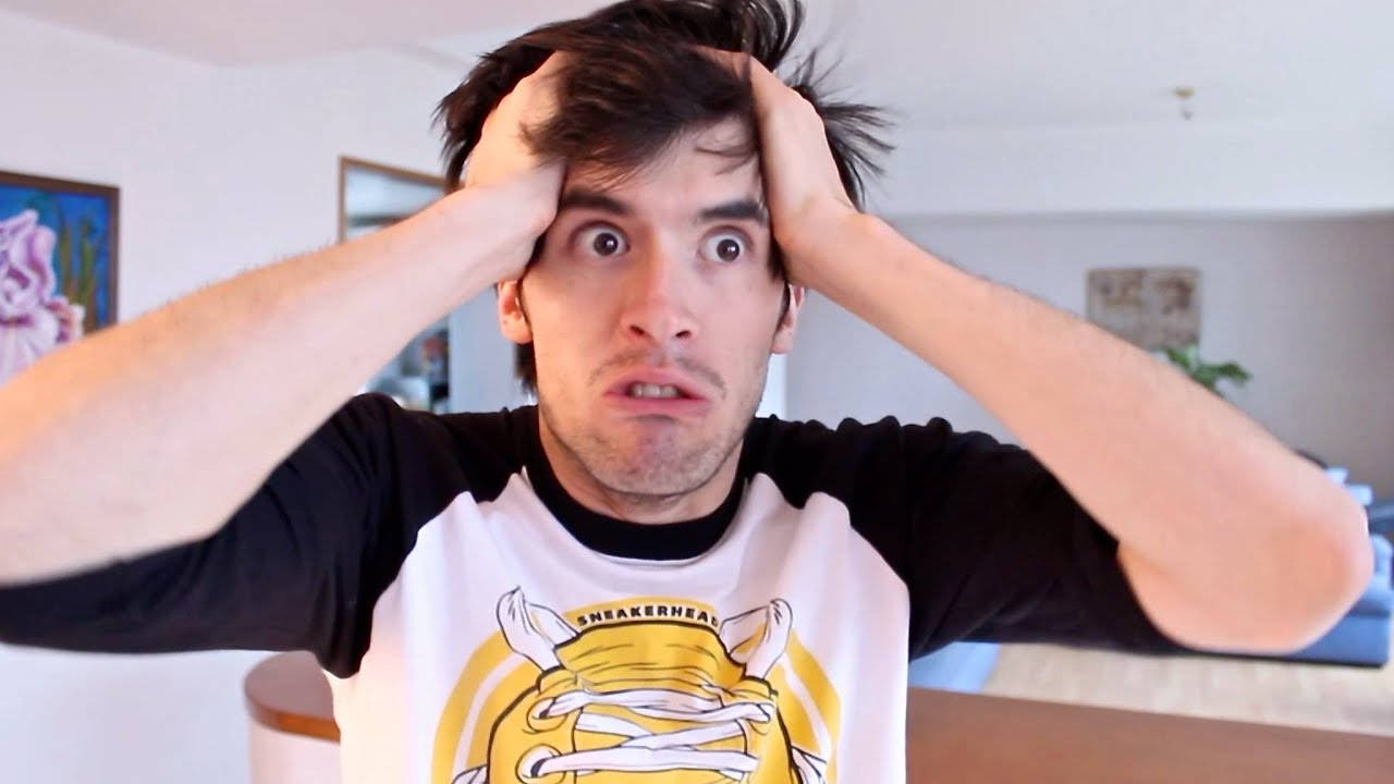 HolaSoyGerman 拉著頭髮 壁紙 — 一個男人瞪大雙眼，雙手放在頭上，在光線明亮的房間裡顯得震驚。