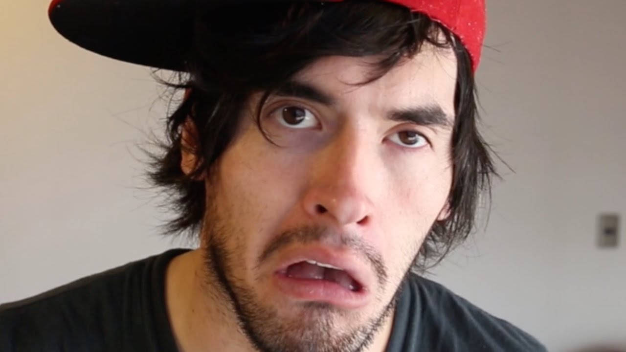 HolaSoyGerman 搞笑表情 壁紙 — 一名深色頭髮、戴紅色帽子的男子在簡單的室內環境中睜大眼睛、張開嘴巴凝視。
