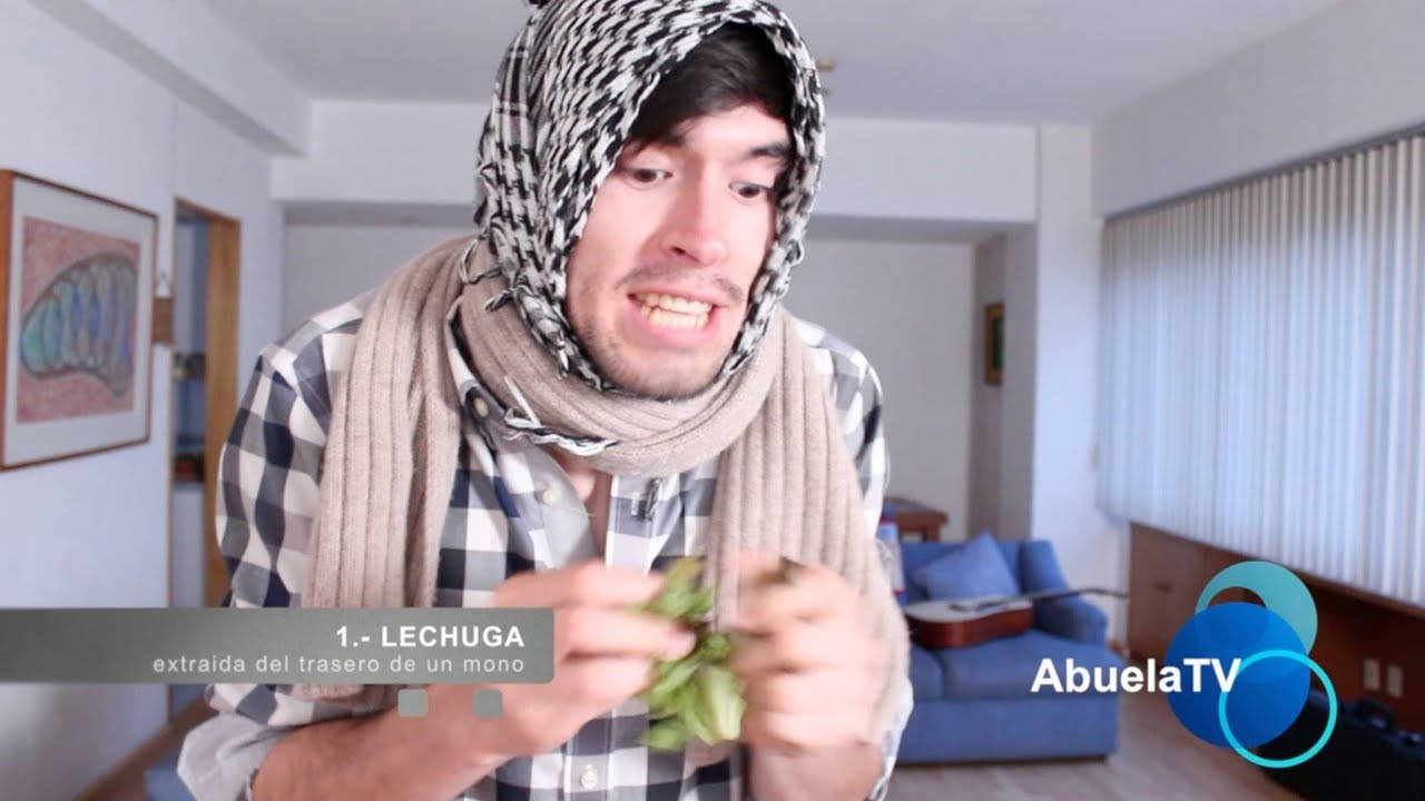 HolaSoyGerman 模仿Abuela TV節目 壁紙 — 一個穿著格仔衫同頭巾嘅男人喺明亮嘅客廳入面拎住一塊綠色葉菜，做出苦面表情。