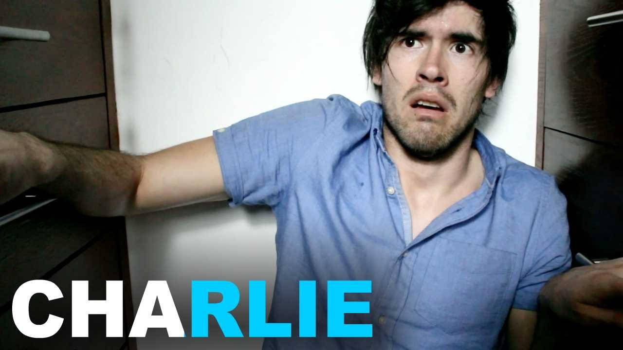 HolaSoyGerman 演Charlie小品 壁紙 — 一名身穿藍色襯衫的男子靠著帶有文字疊加的牆壁，露出驚嚇的表情。