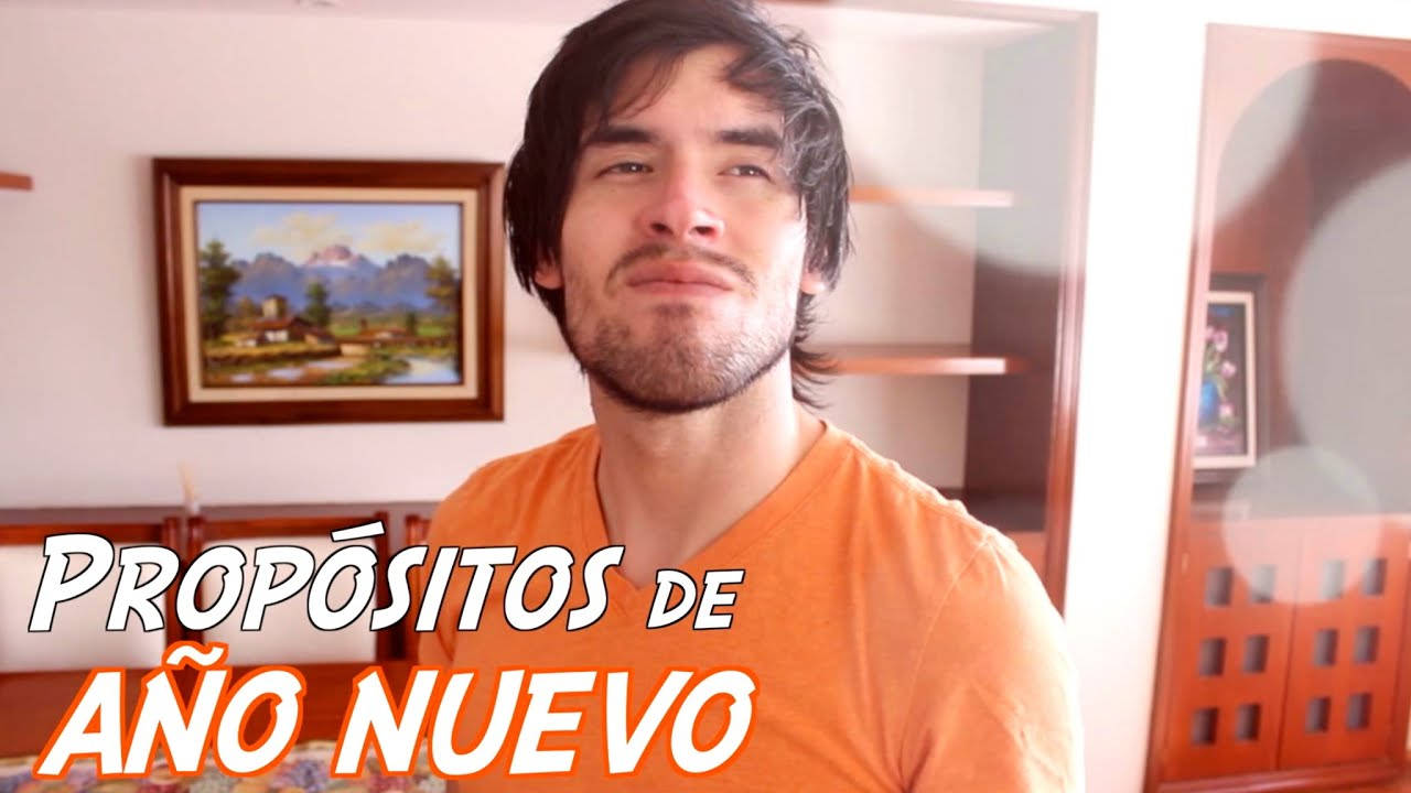 HolaSoyGerman 神情堅定 壁紙 — 一名身穿橙色襯衫的男子在室內微笑，身後有一幅裱框的山景畫。