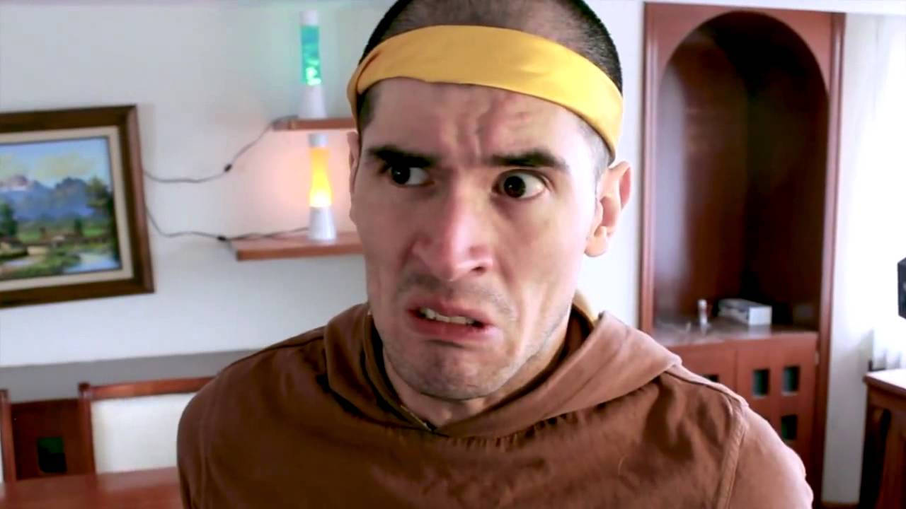 HolaSoyGerman 立體皺眉表情 壁紙 — 一個戴著黃色頭帶的男人在溫暖照明的房間裡，睜大眼睛、表情扭曲，震驚地凝視著。
