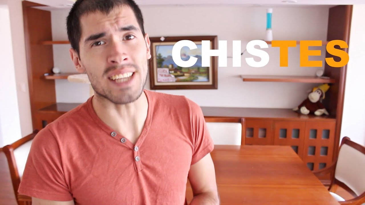 HolaSoyGerman 粉紅襯衫 壁紙 — 一名身穿紅色襯衫的男子在一個有木製家具和猴子毛公仔的飯廳裡對著鏡頭做鬼臉。