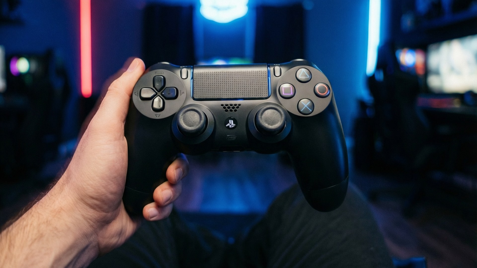 手在霓虹燈遊戲室中握著黑色PlayStation控制器