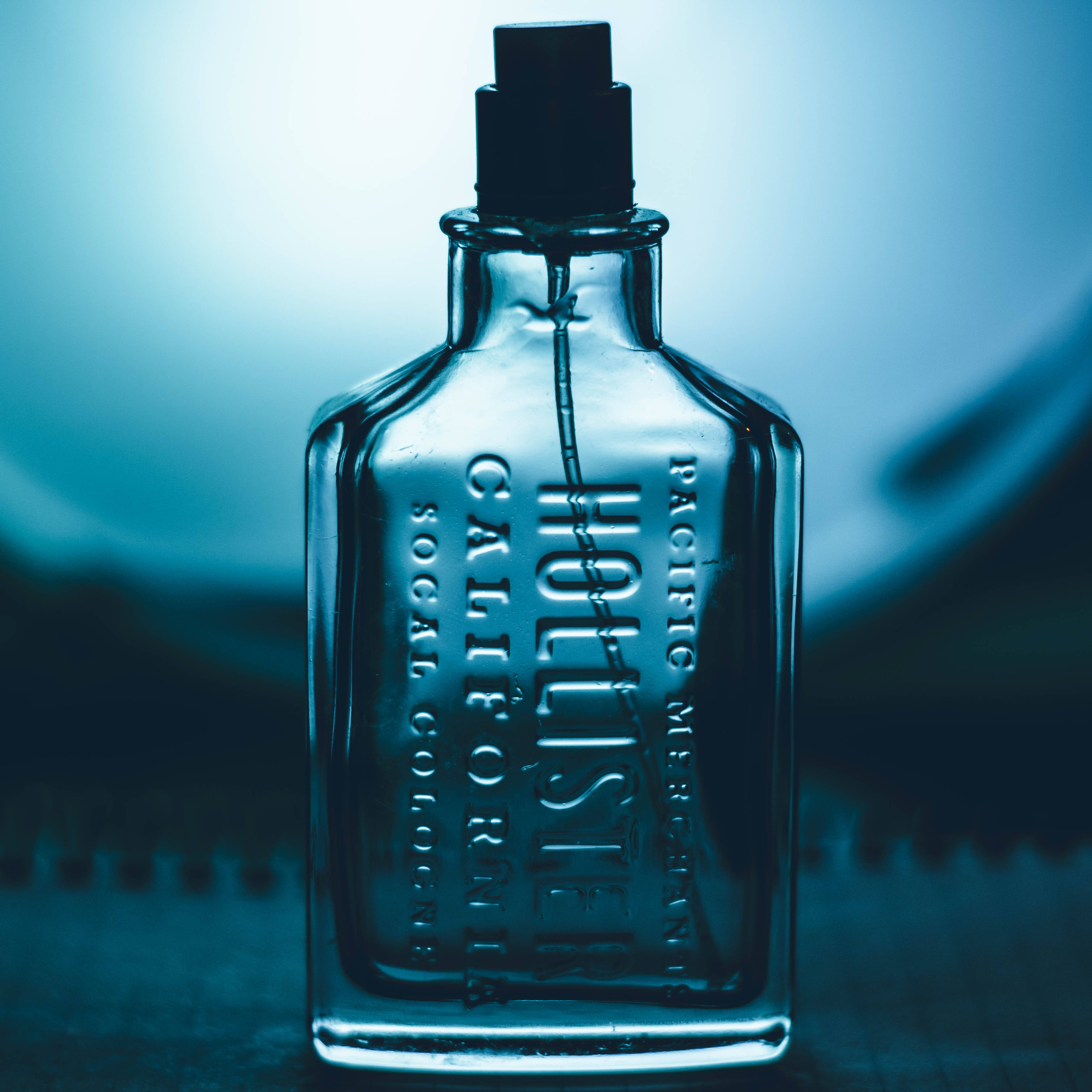 Hollister 雕刻香水瓶 壁紙 — 一個帶有浮雕文字的復古玻璃古龍水瓶，居中放置在柔和的藍色漸變背景上。