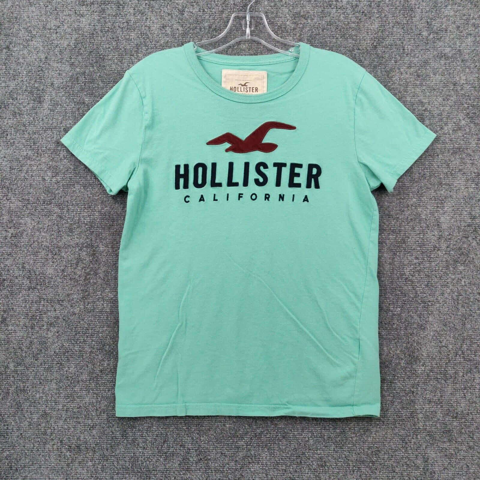 薄荷綠色Hollister T恤，紅色海鷗標誌，掛在衣架上。